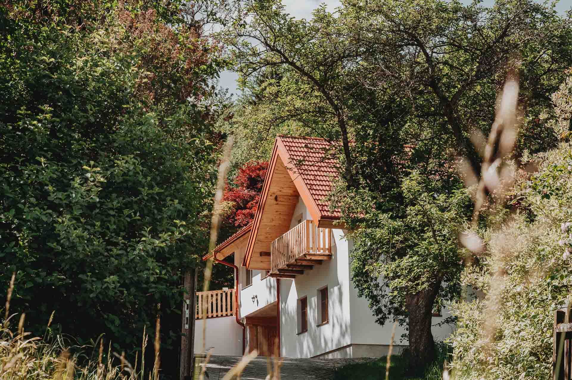 A white house with a red tiled roof, surrounded by trees and plants.