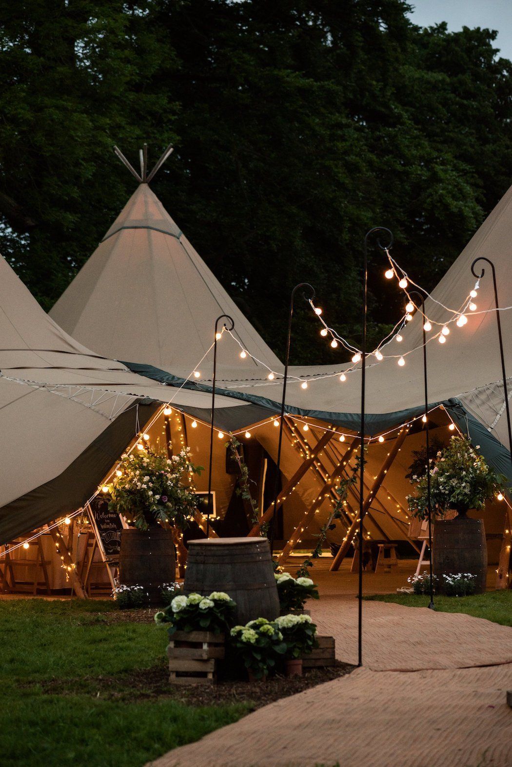 An illuminated teepee tent for an event, surrounded by plants and fairy lights.