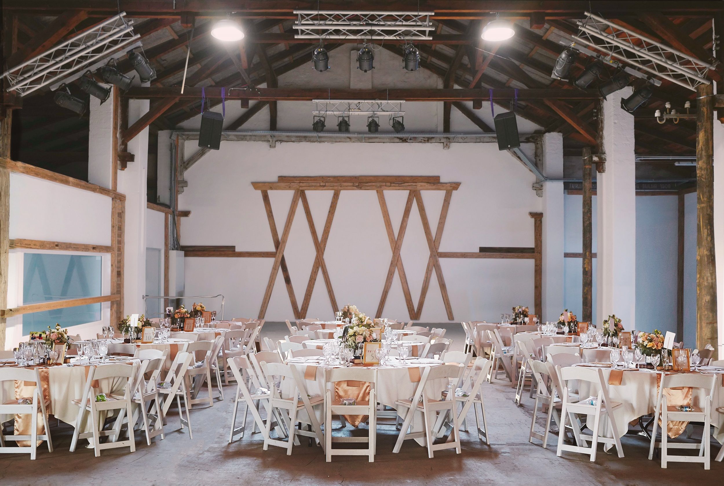 Interior view of a stylishly decorated event hall with round tables and white chairs.