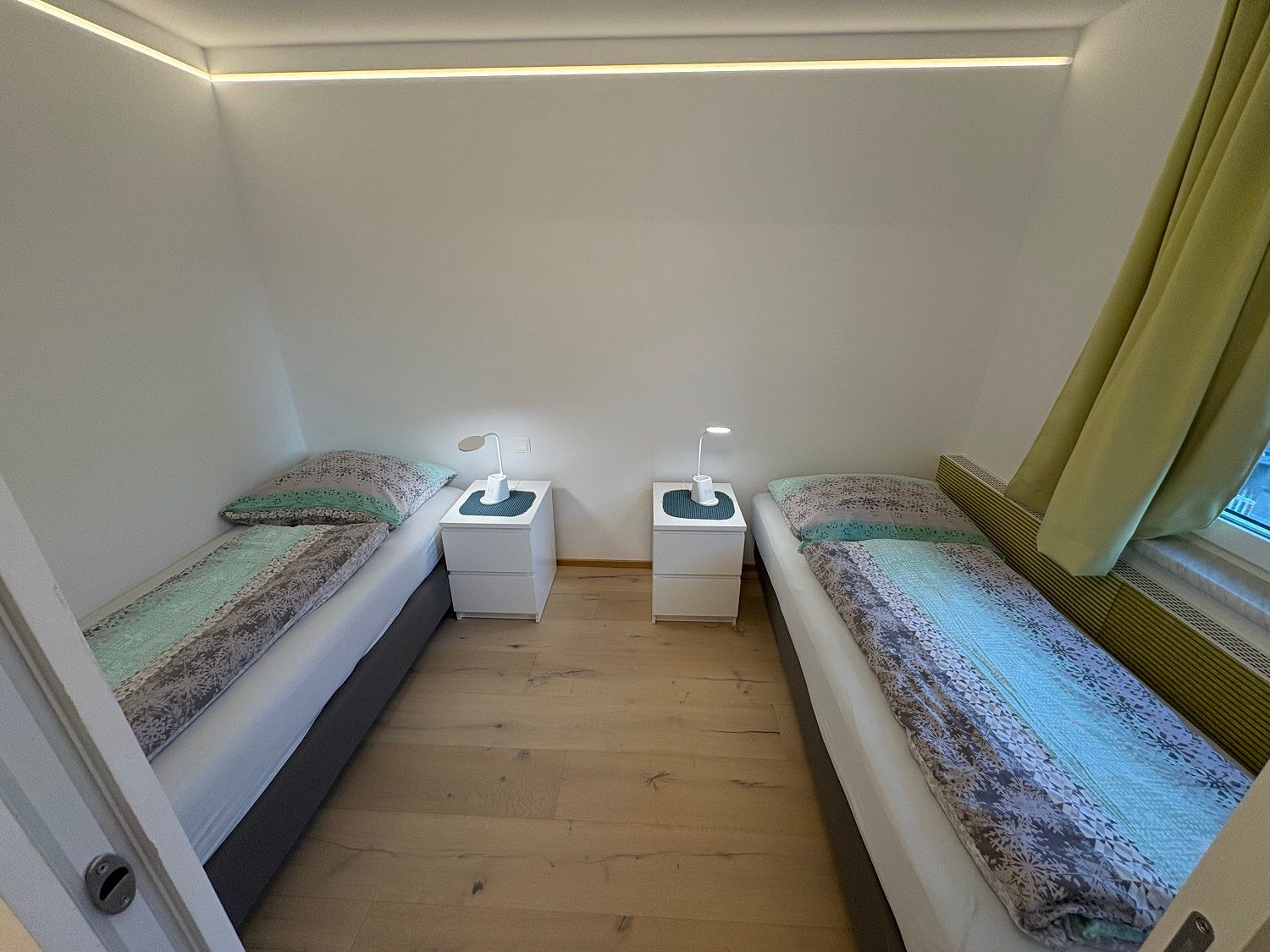 Bedroom with two single beds, bedside table and lamps.