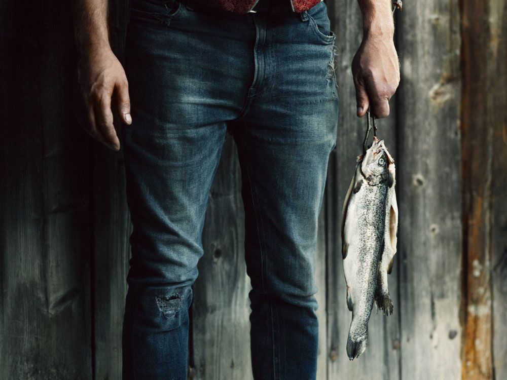 Person holding a trout in front of a wooden wall.