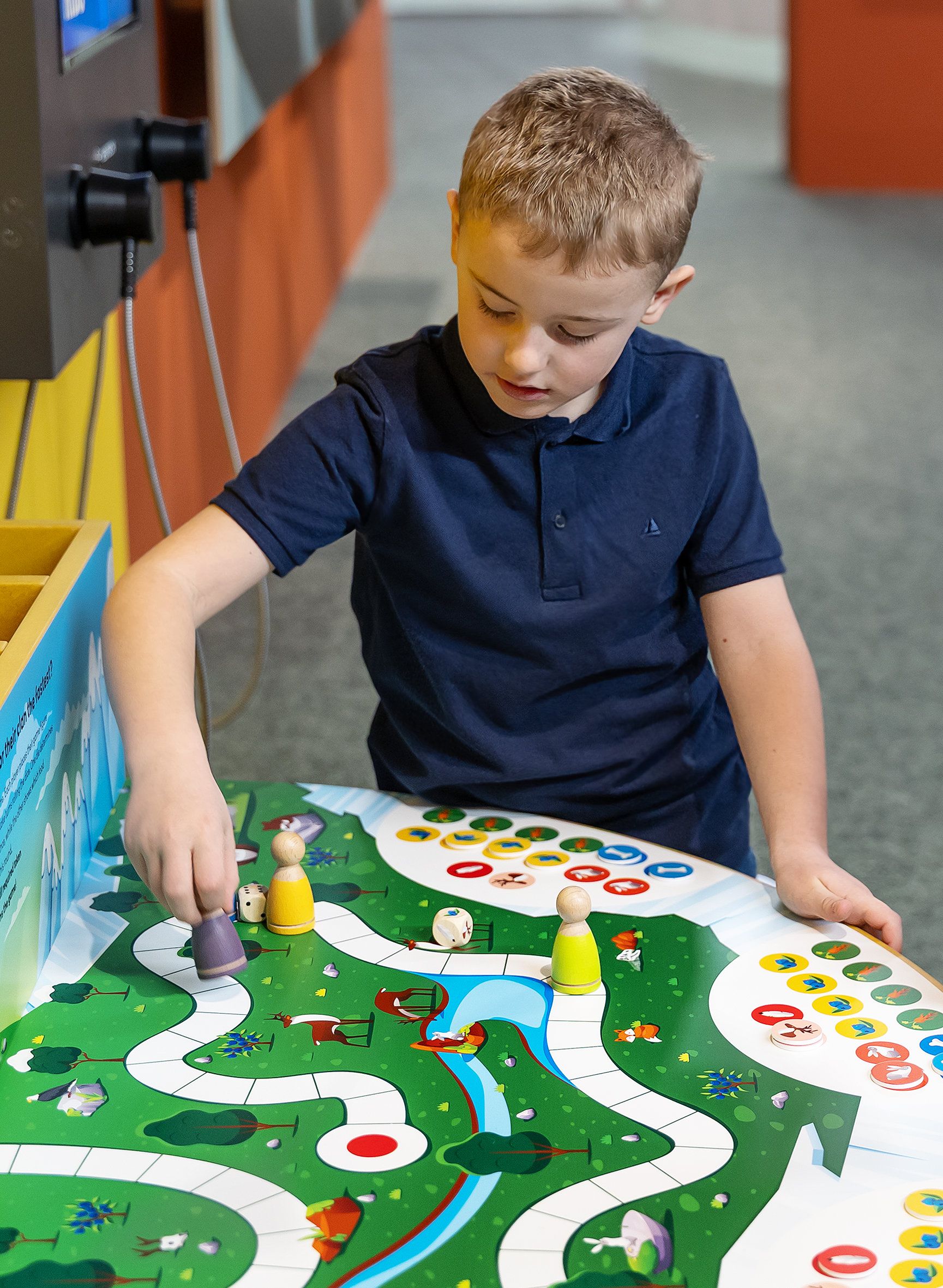 A child plays a board game with colorful game pieces and dice on a table.