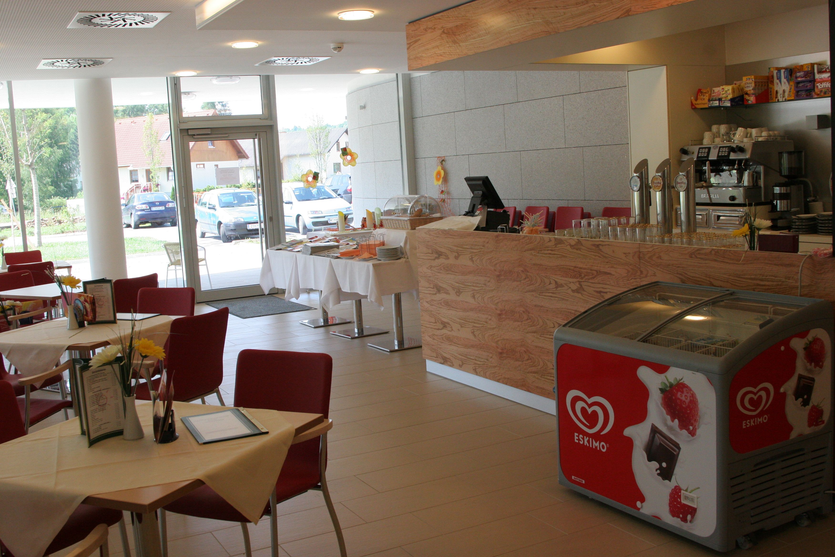 Interior view of a café with red chairs, wooden counter and ice cream freezer.