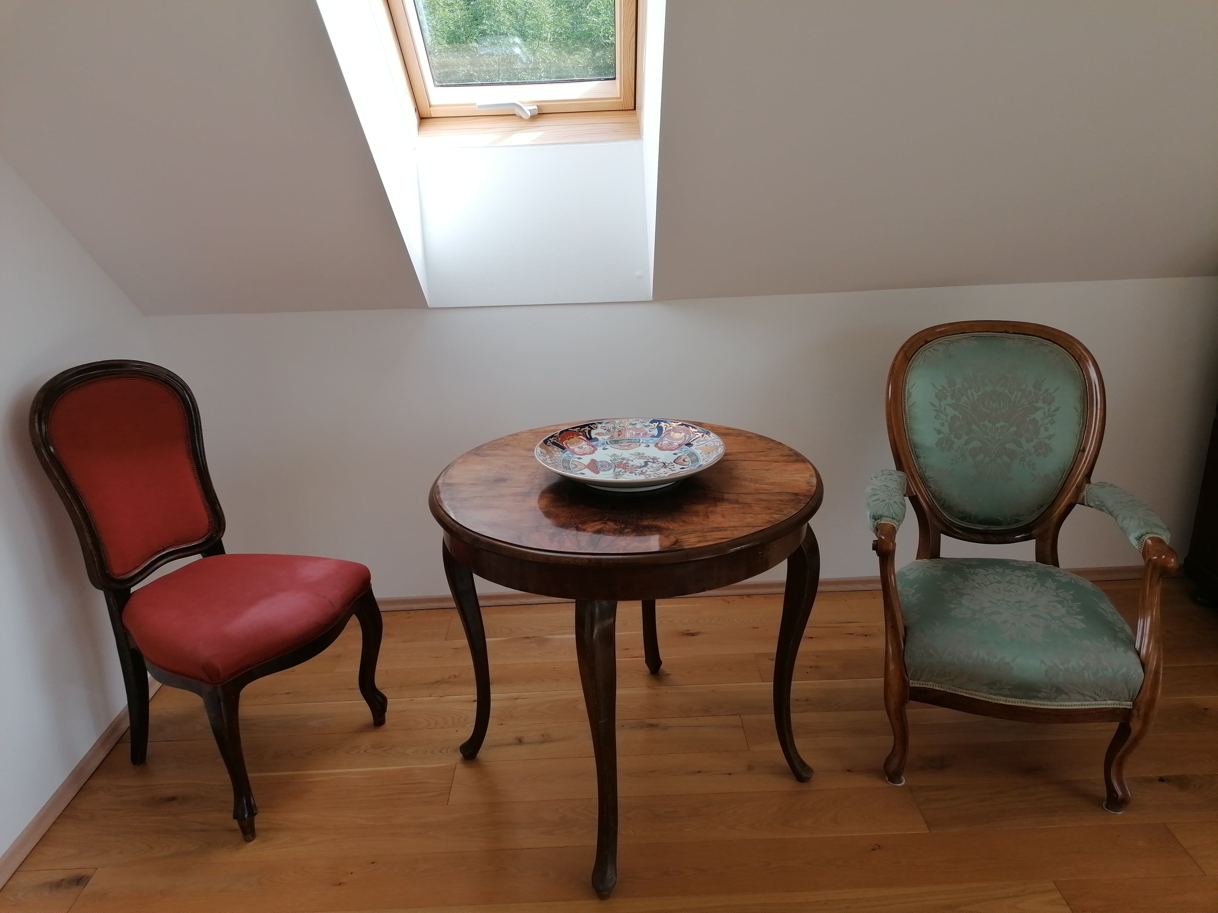Two antique chairs and a round wooden table with a decorative bowl in a room with a skylight.