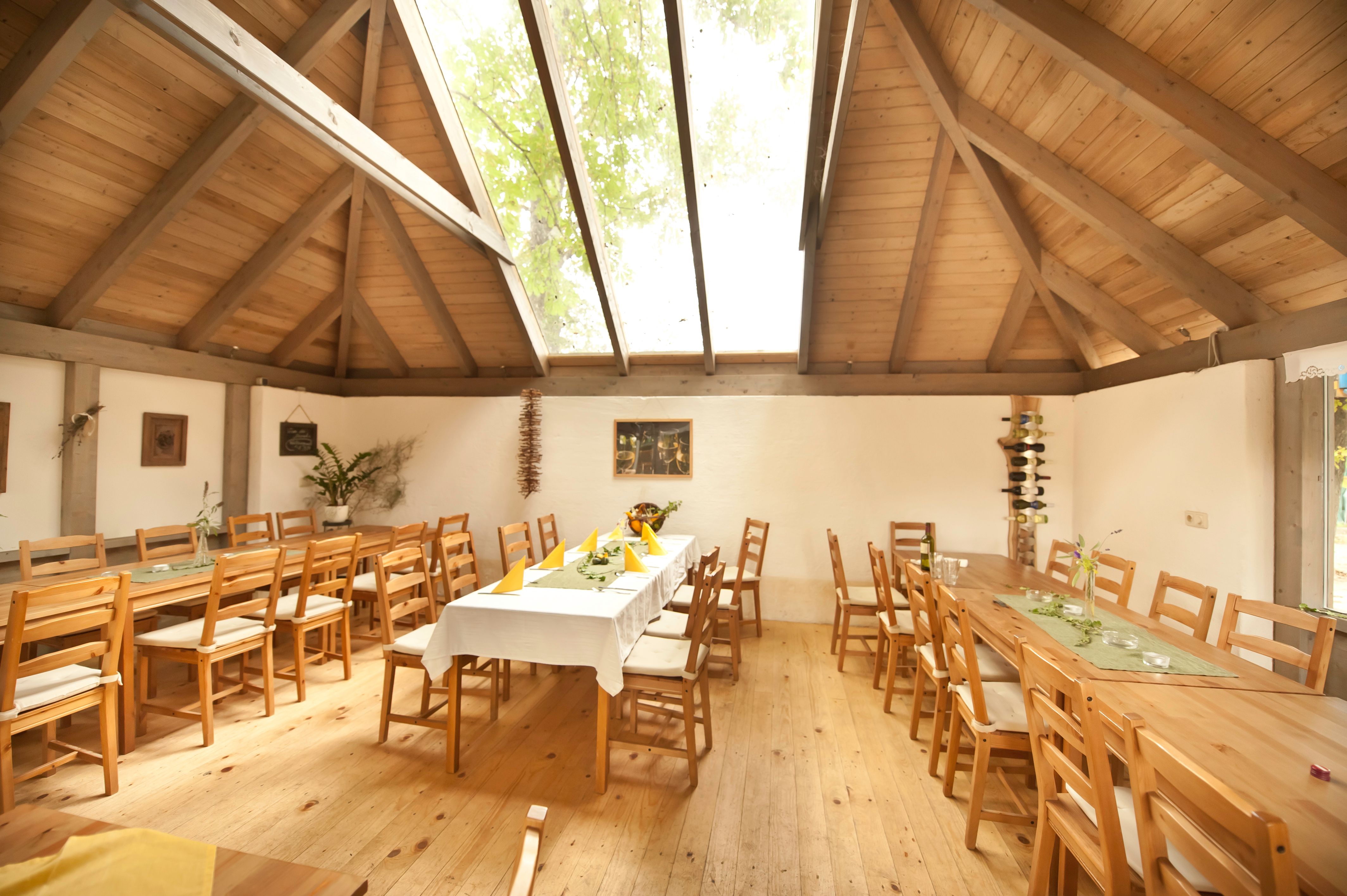 Interior view of a rustic room with wooden tables and chairs, a large skylight and decorative plants.