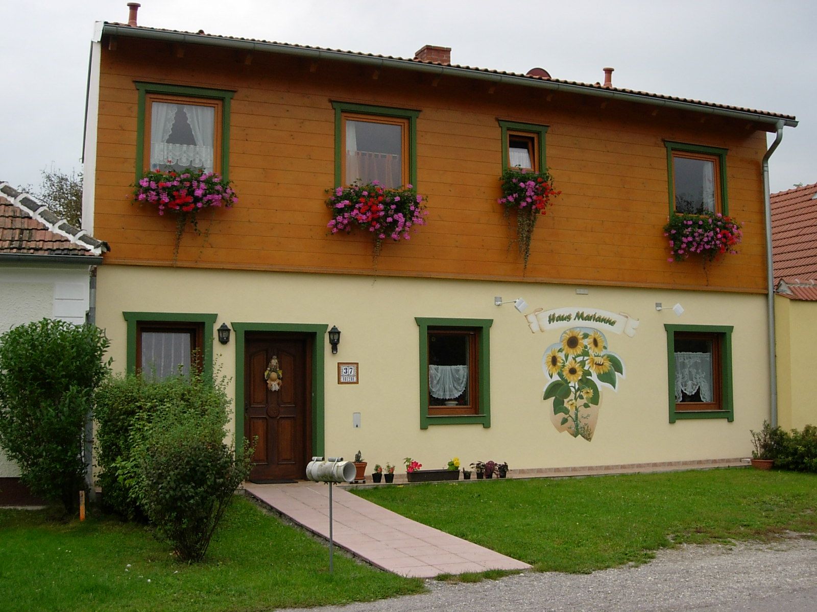 Two-storey house with wooden cladding and flower boxes, labeled 'Haus Marianne'.