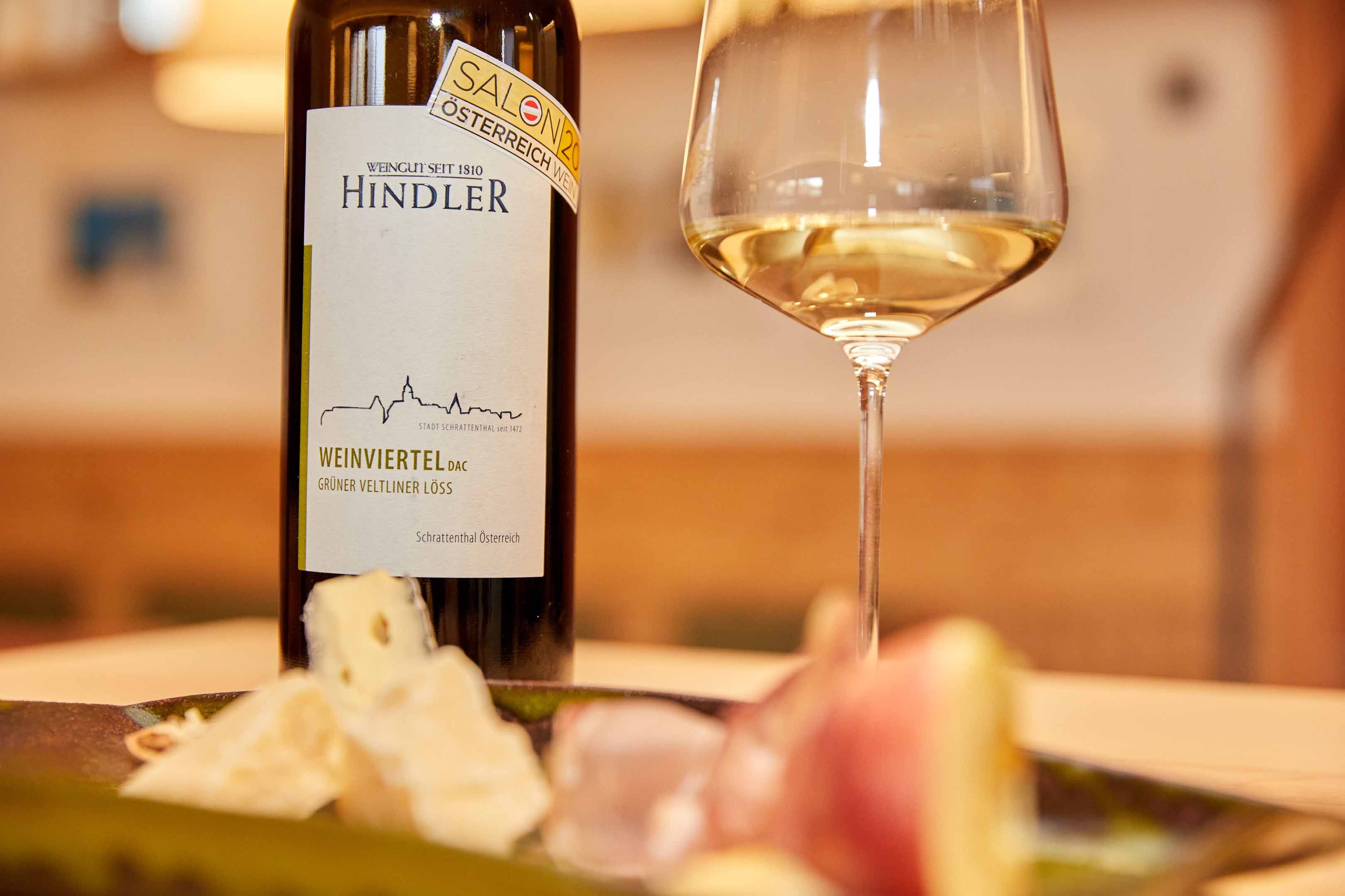 Wine bottle and glass with white wine, cheese and ham in the foreground.