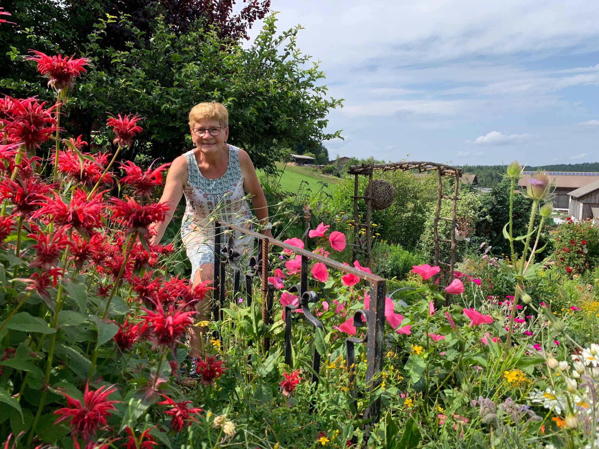 Woman in a blooming garden with red and pink flowers.