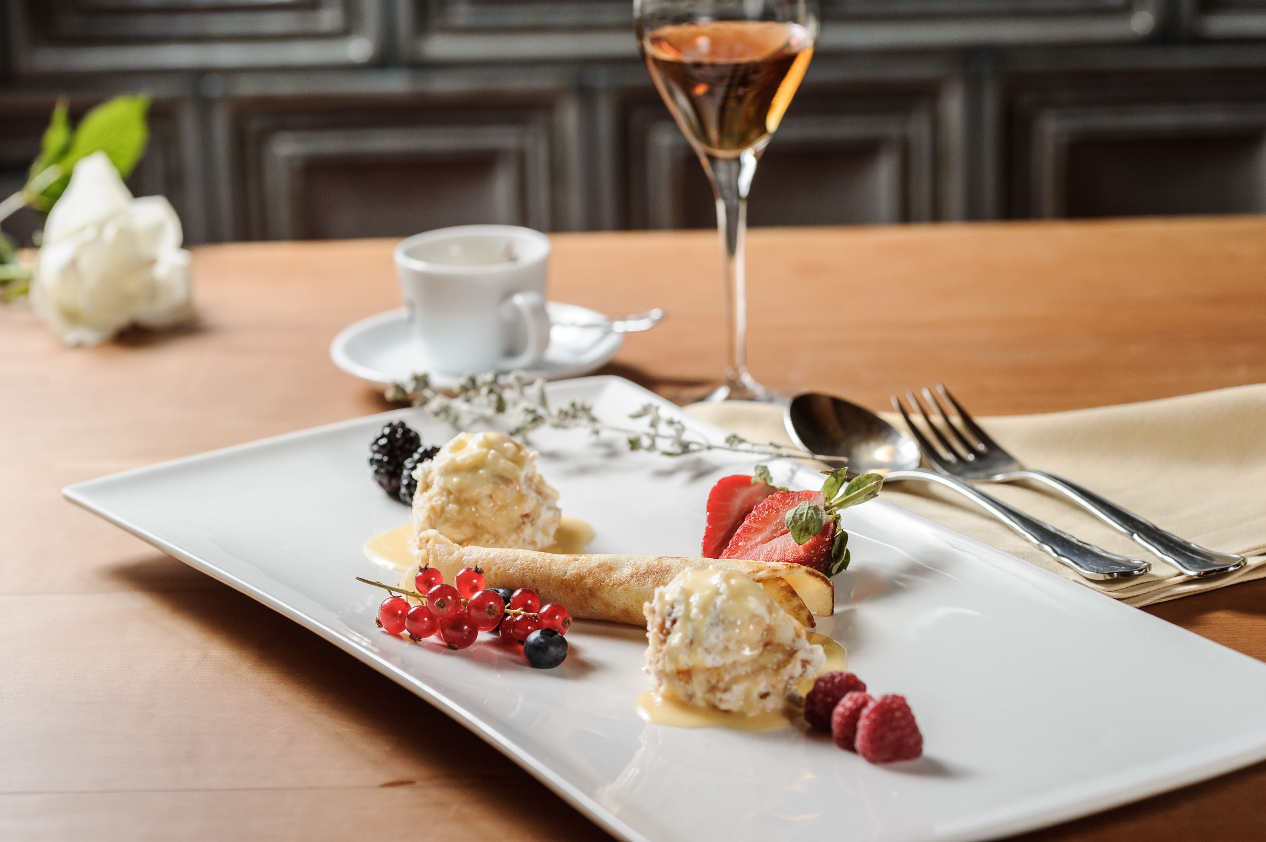 Elegant dessert with fruit and ice cream on a white plate, accompanied by a glass of wine and a cup of coffee.