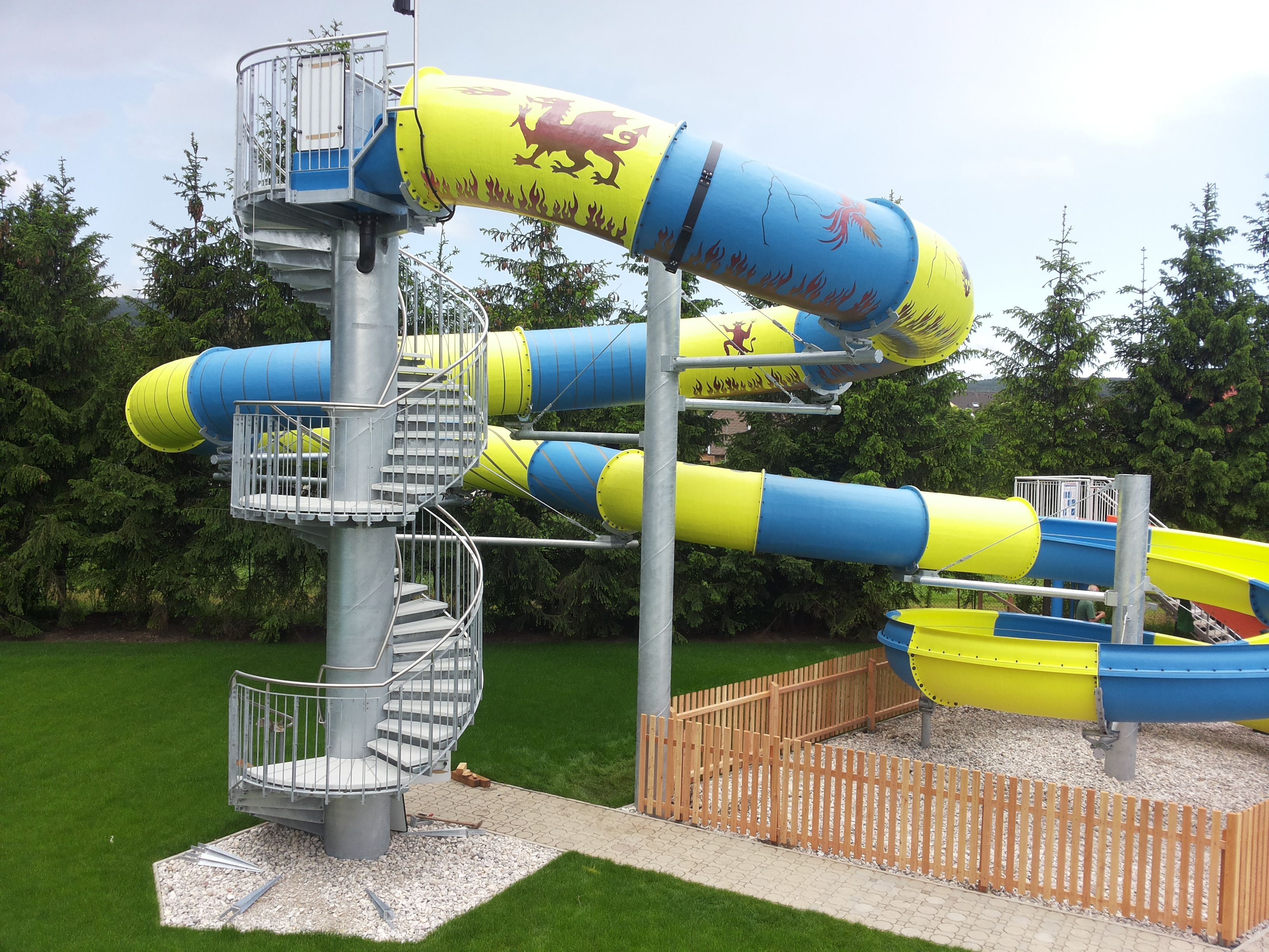 Large water slide with blue and yellow tubes and spiral staircase.