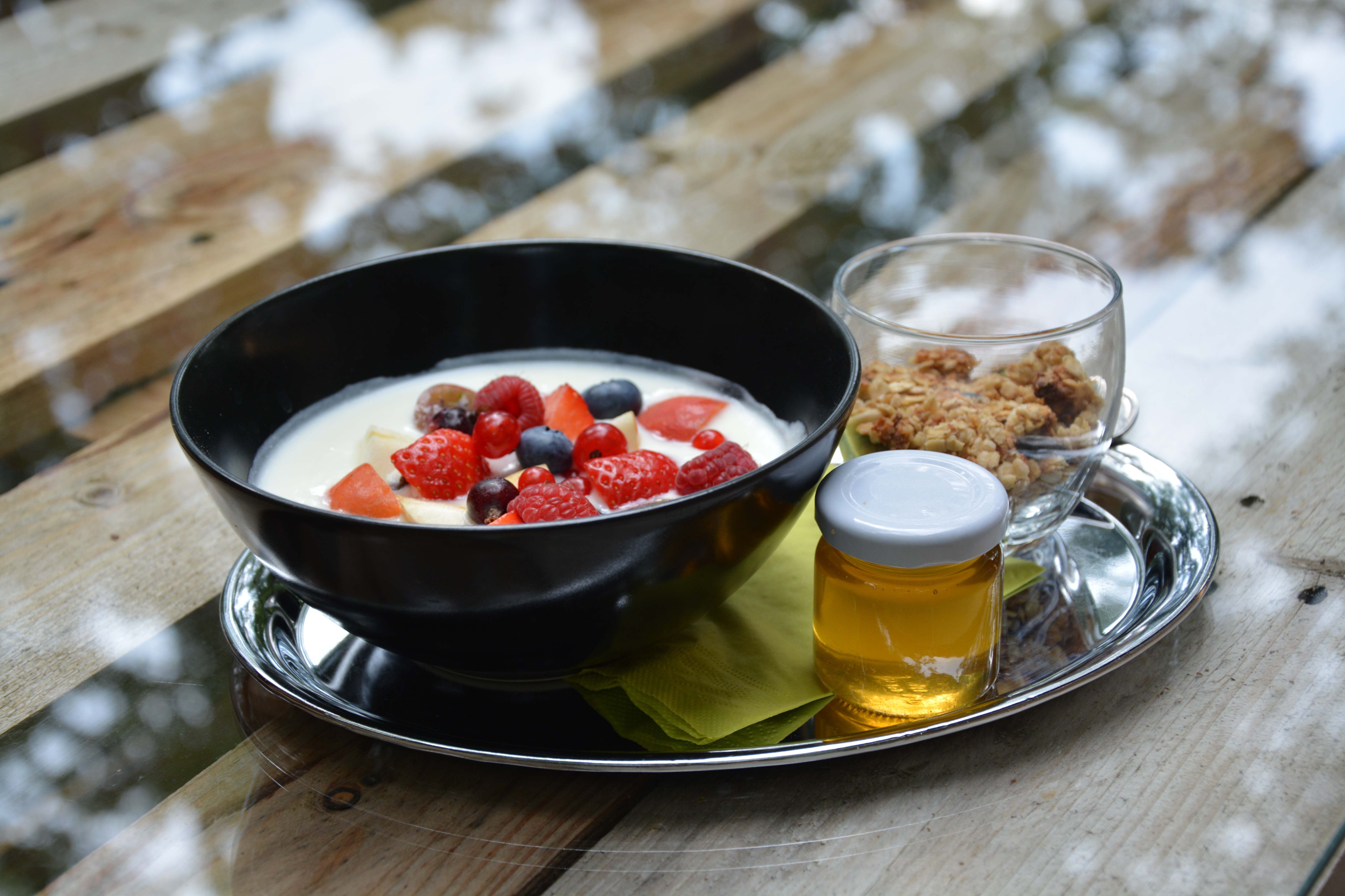 Black bowl with yogurt and berries on a silver tray with honey and muesli.