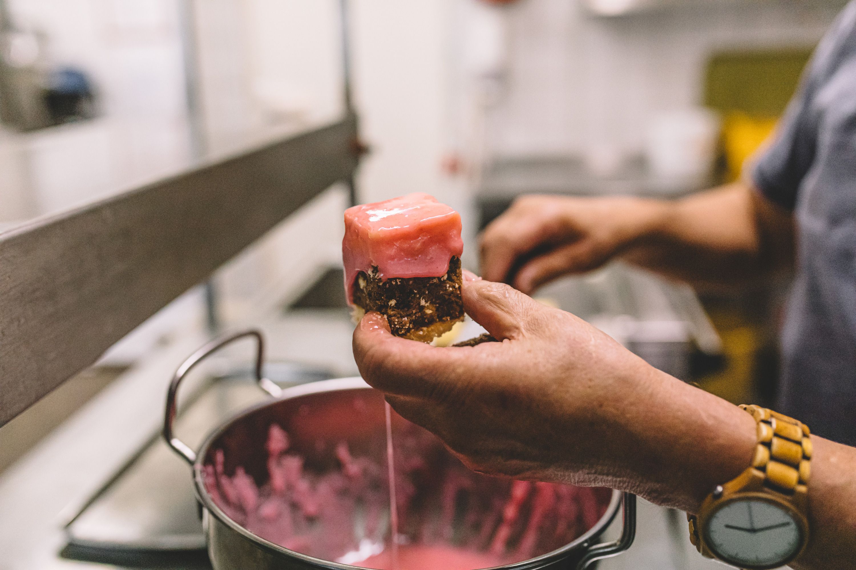 Person holding a piece of pastry with pink icing over a pot.