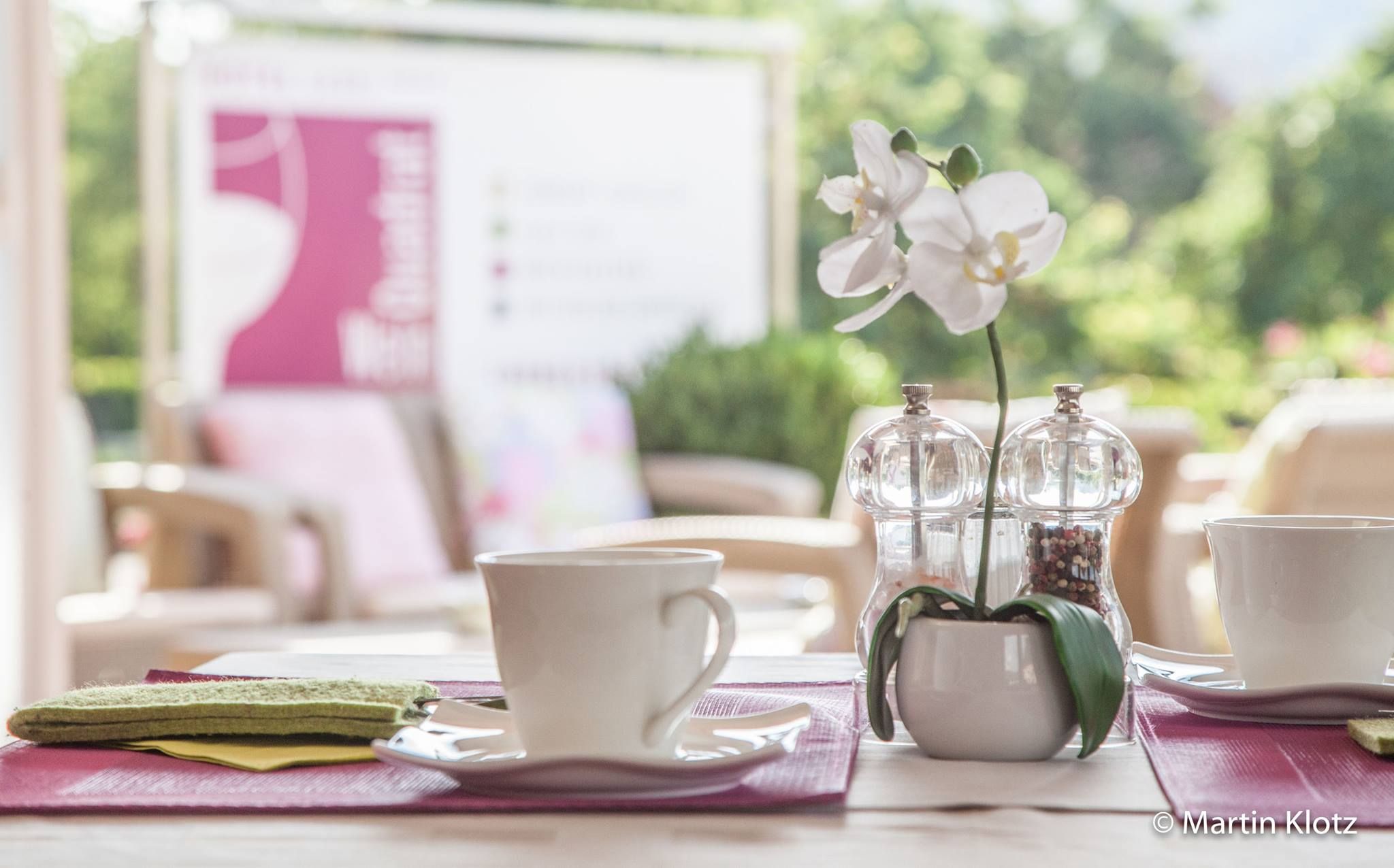 A laid table with two cups, salt and pepper shakers and a white orchid in the foreground.