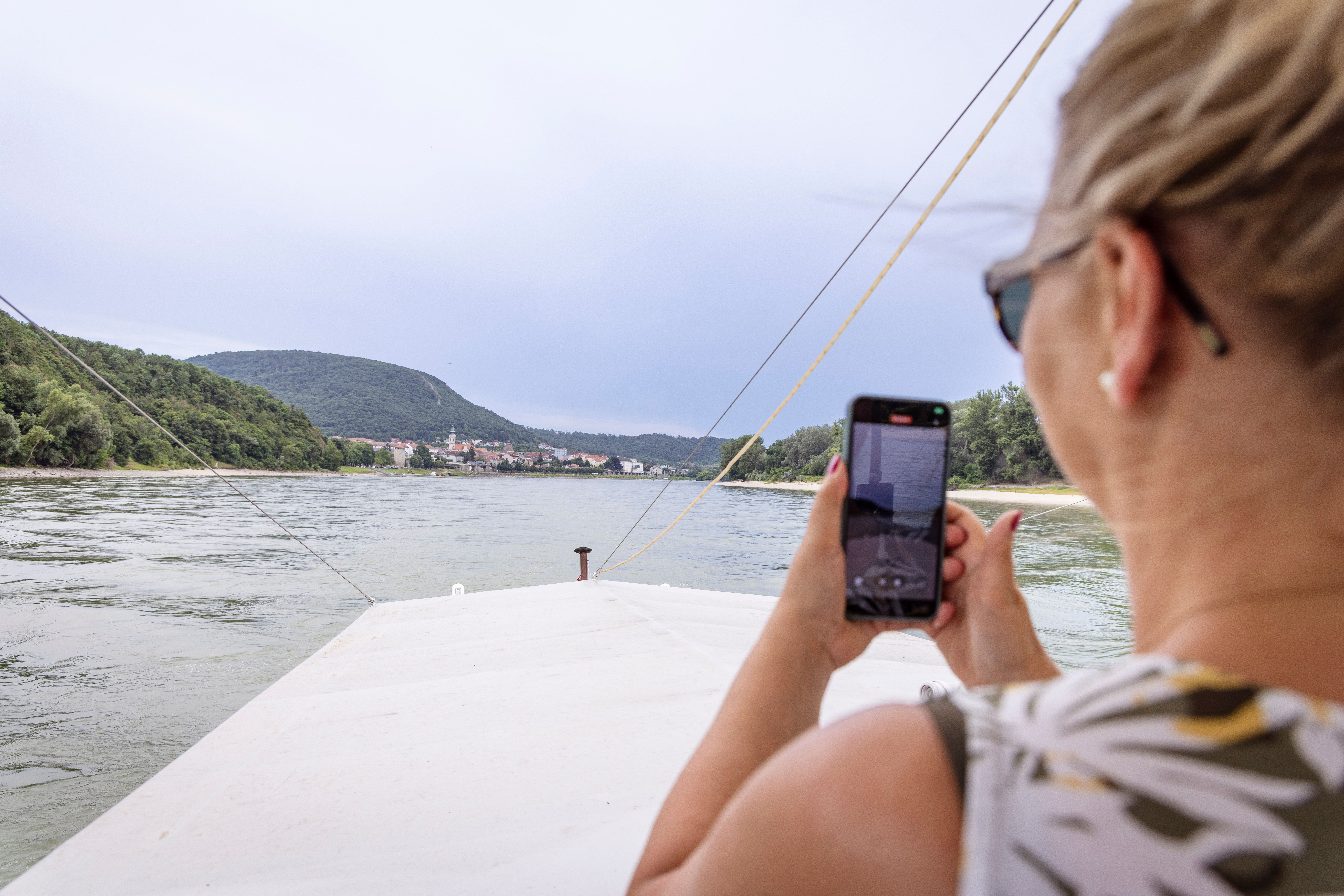 Woman on a boat takes a photo of the Danube with her cell phone.