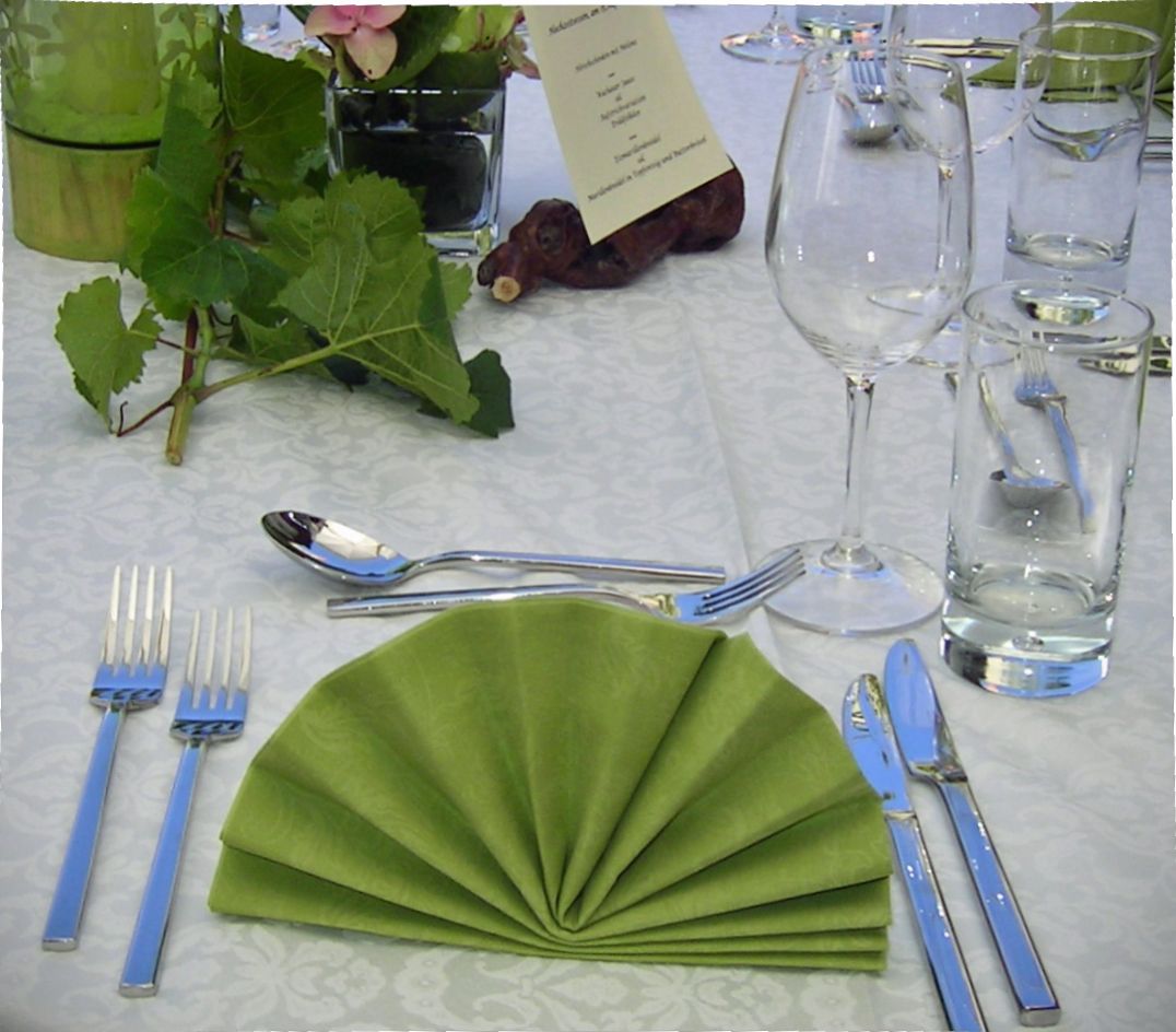 Elegant table decoration with green folded napkin, cutlery, wine glass and water glass on a white tablecloth.