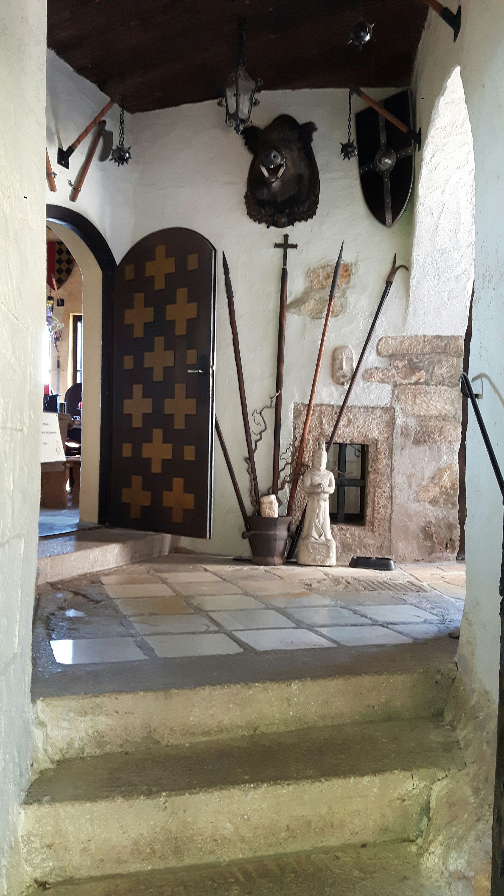 Interior view of a castle with weapons, a boar's head and a statue.