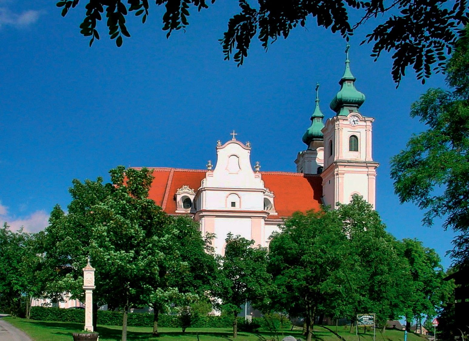 Maria Dreieichen Basilica with red roofs and green towers, surrounded by trees.