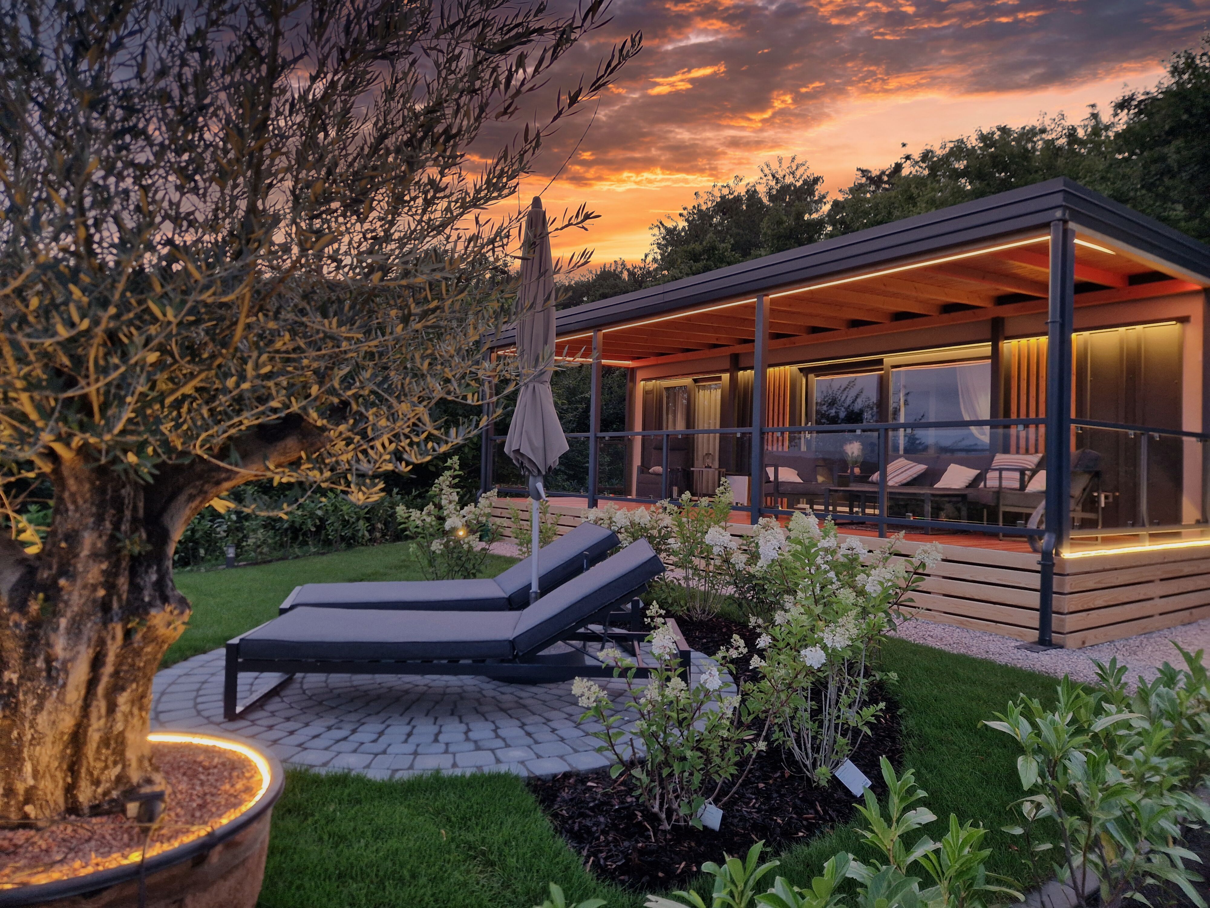 A modern chalet with terrace and sun loungers in the garden at sunset.
