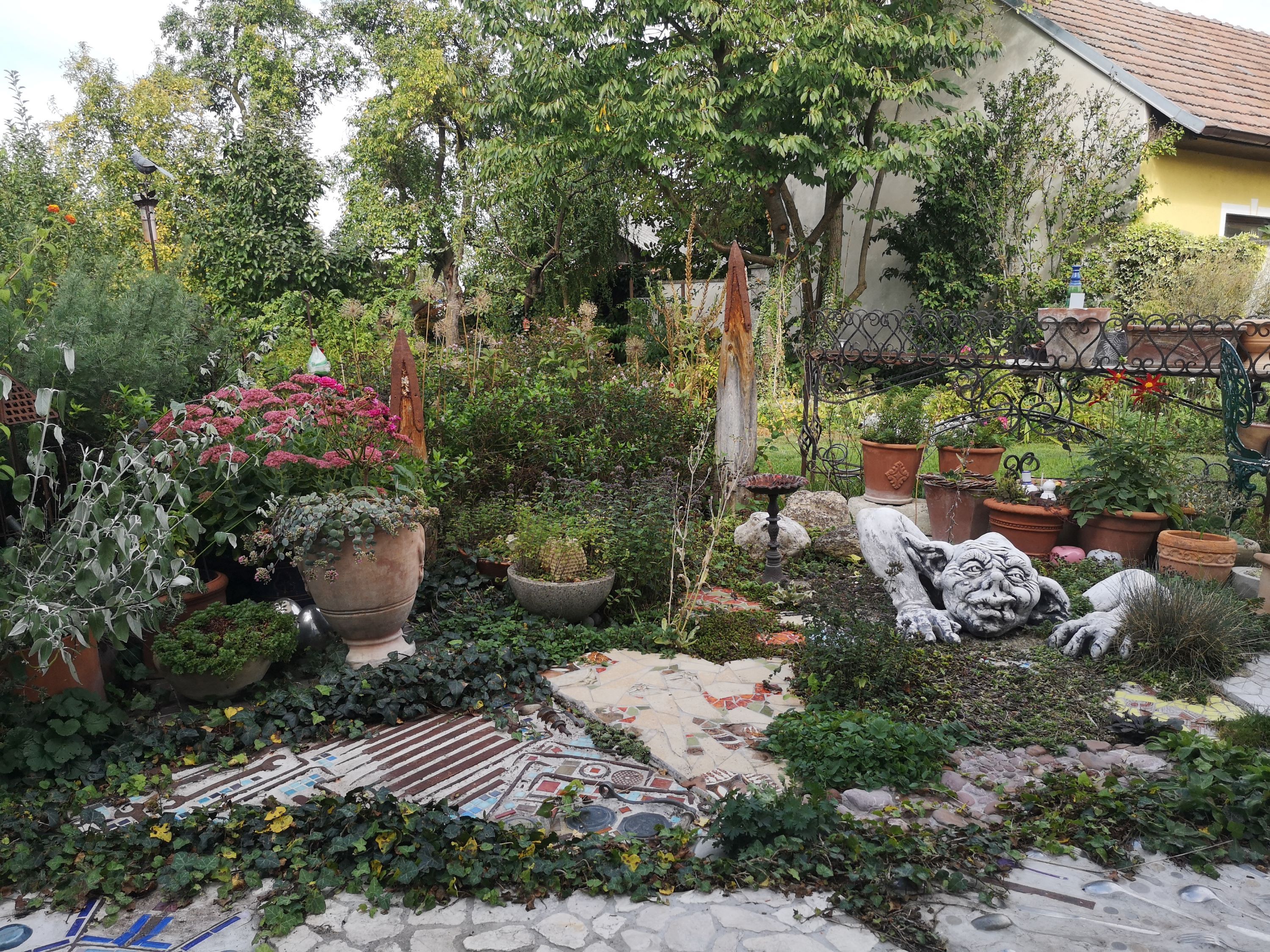 A garden with plants, pots and a grotesque stone sculpture.