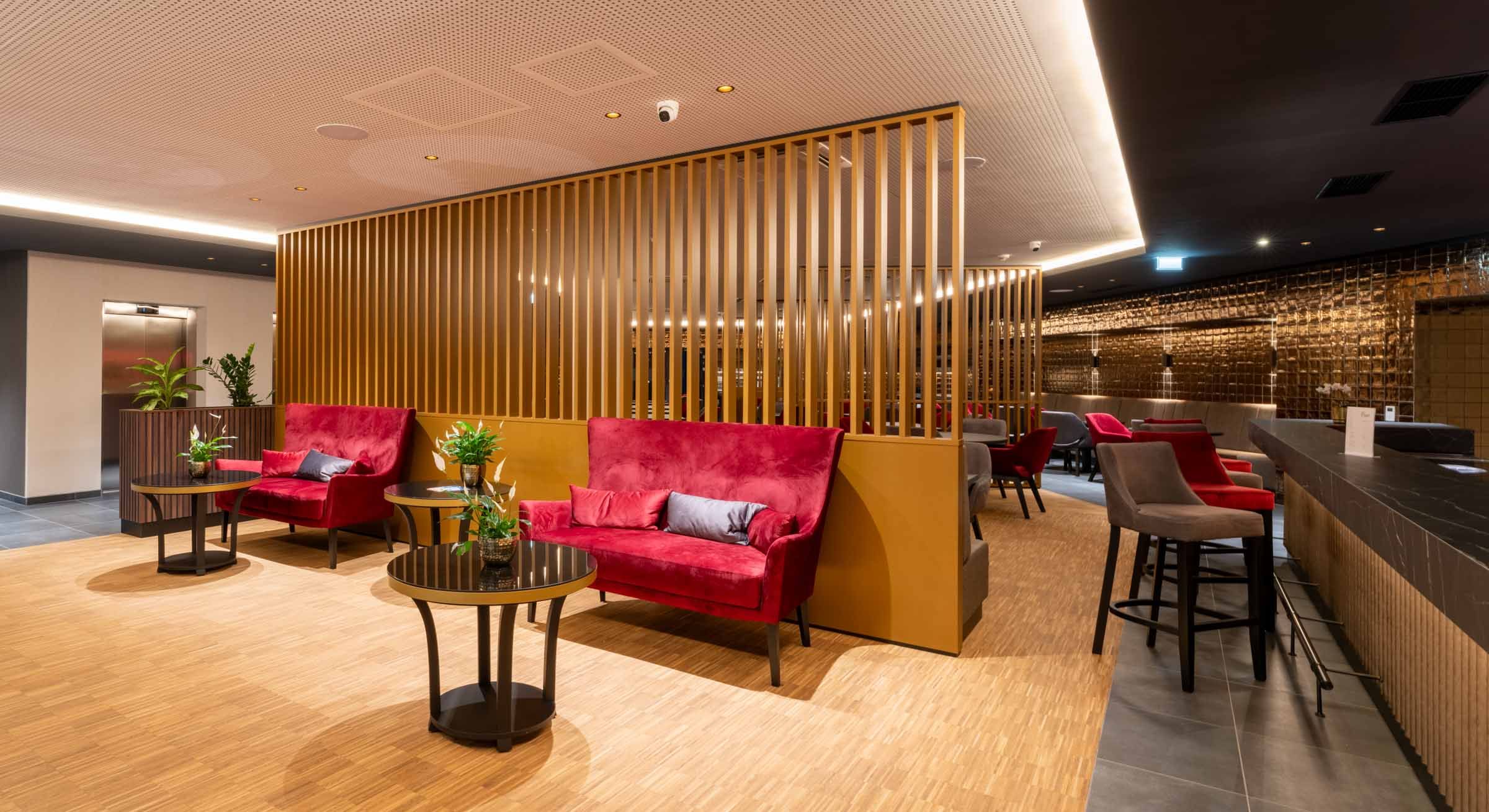 Modern hotel lobby with red sofas, wooden walls and plants.