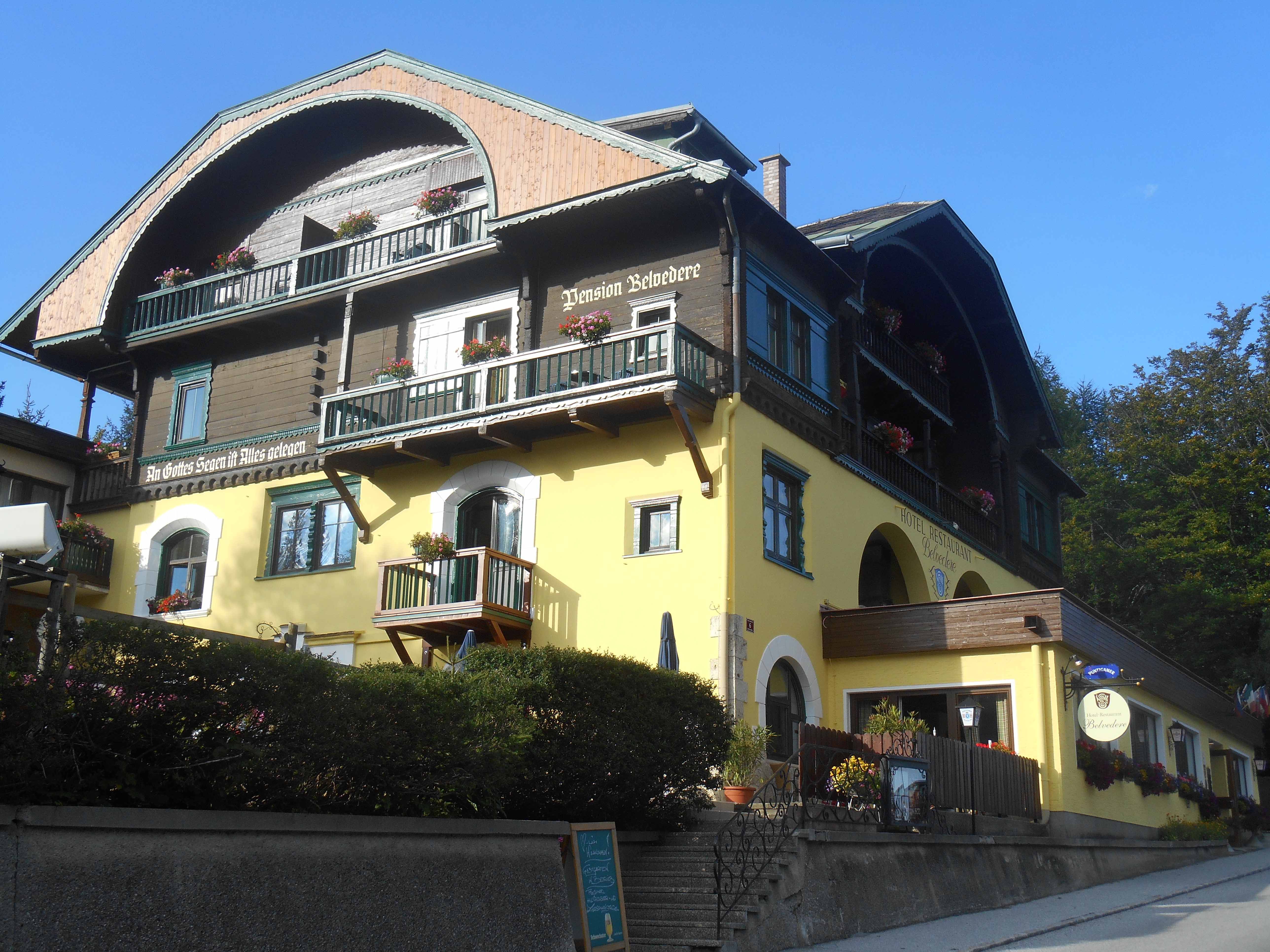 A traditional hotel with a yellow façade and wooden balconies, decorated with flowers.