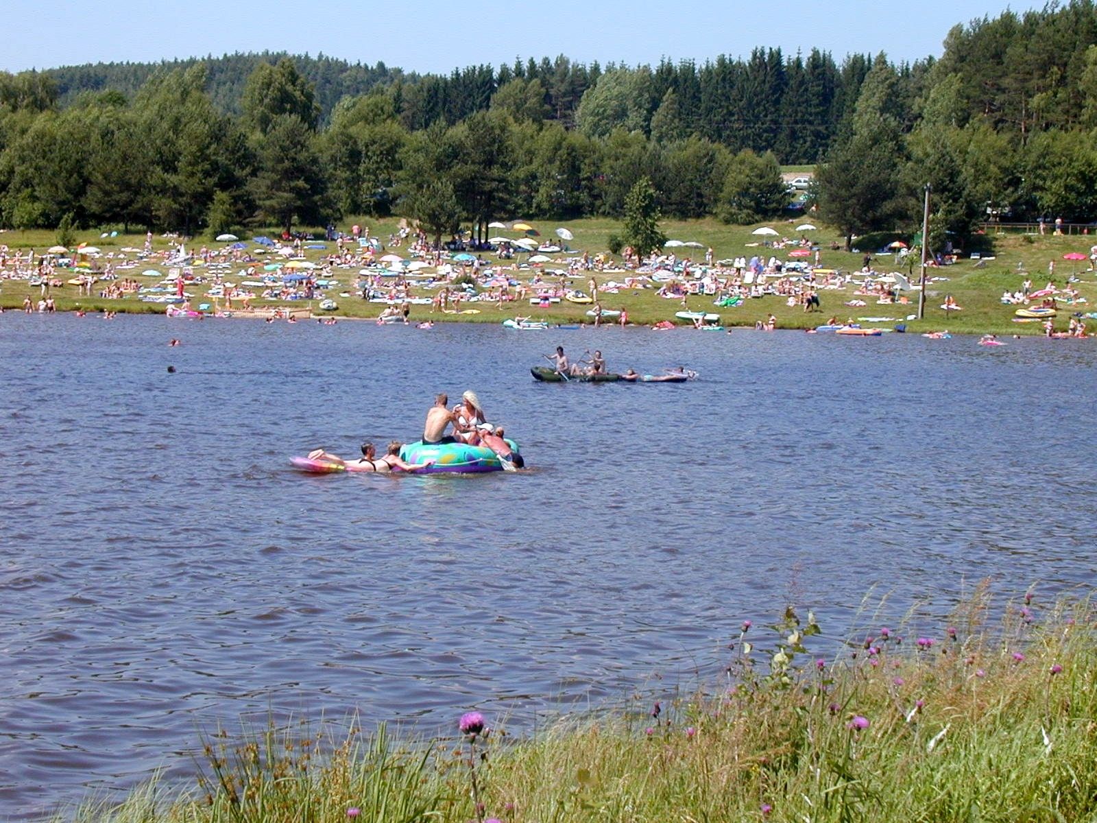People relax by the Frauenwieserteich pond with sun loungers and parasols.