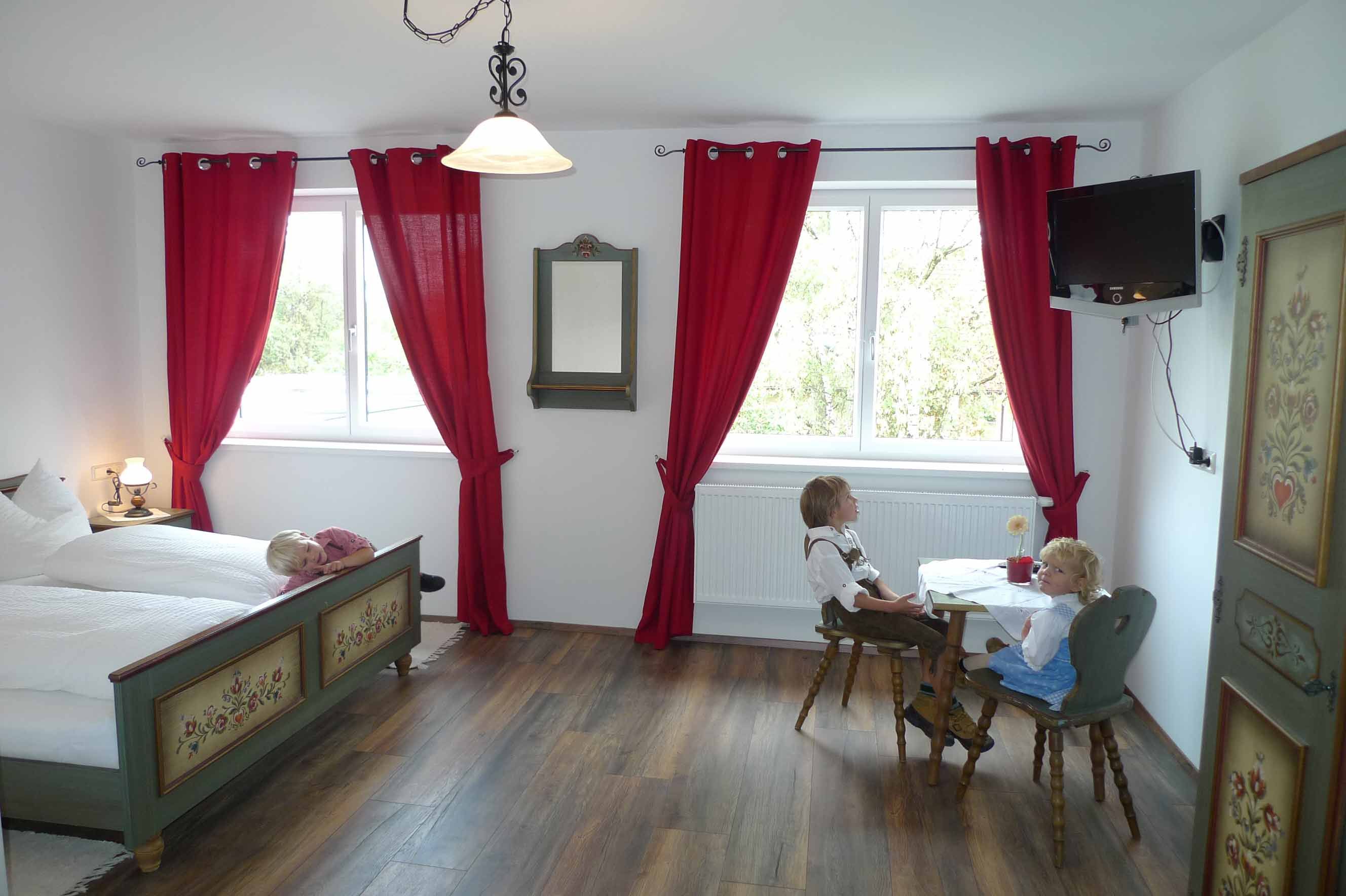 A traditionally furnished room with a wooden floor, red curtains and a table with two dolls in traditional costume.