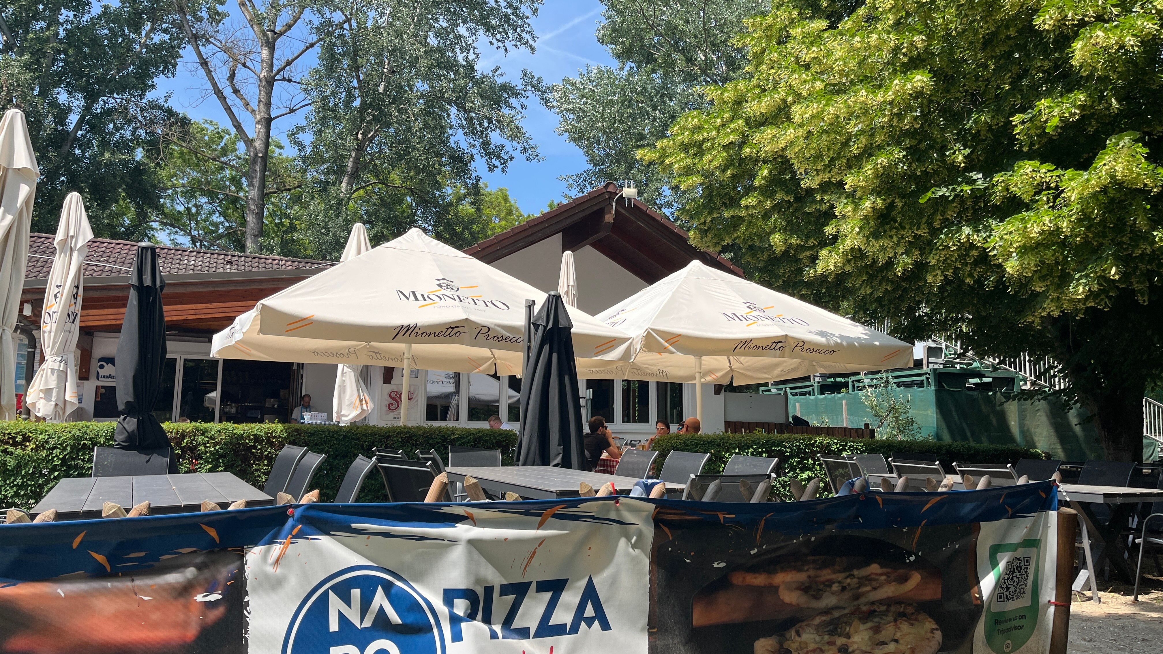 Guest garden with a view of the pizzeria building, trees in the background.