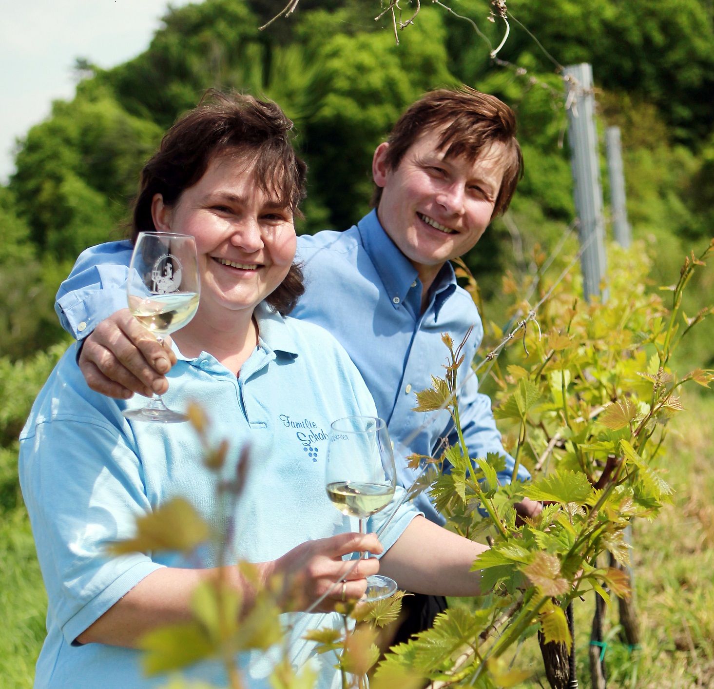 Two people in a vineyard with wine glasses.