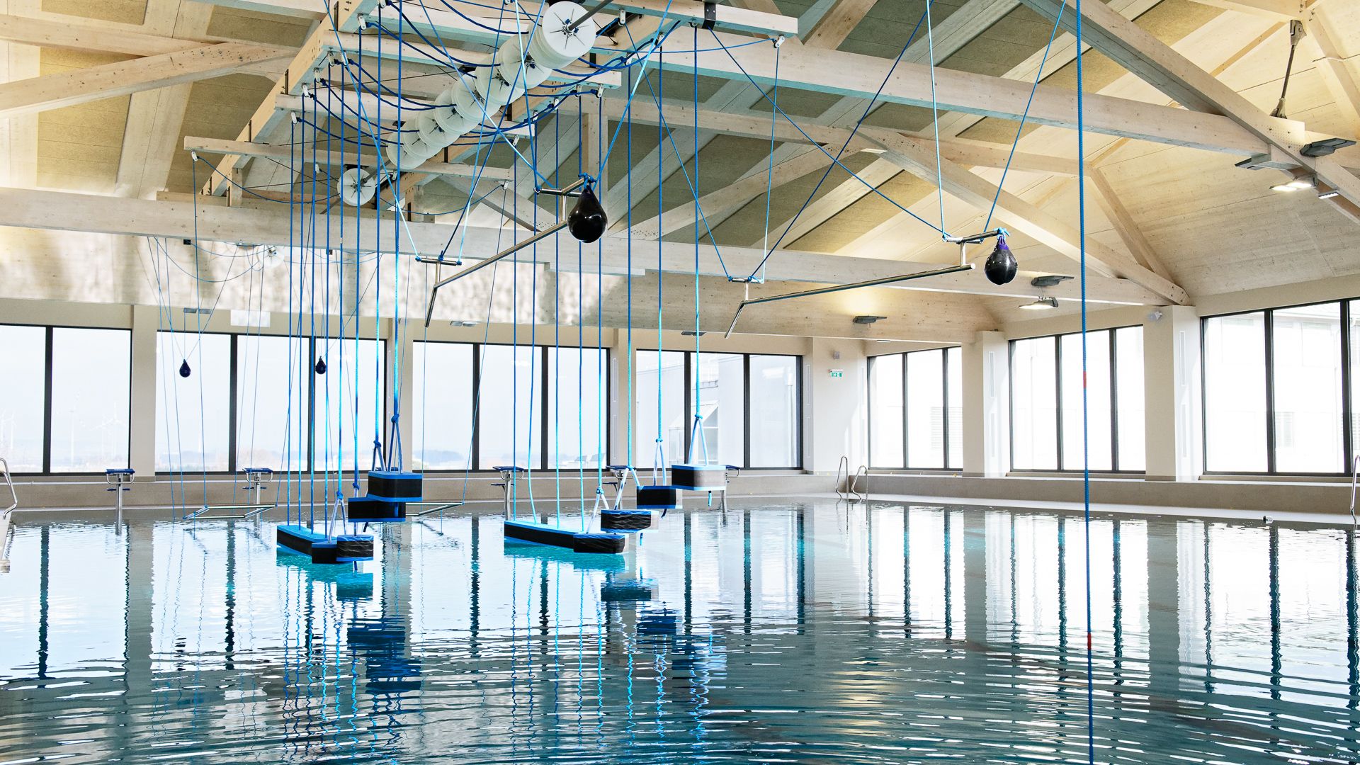 Interior view of a modern swimming pool with hanging blue ropes and platforms above the water.