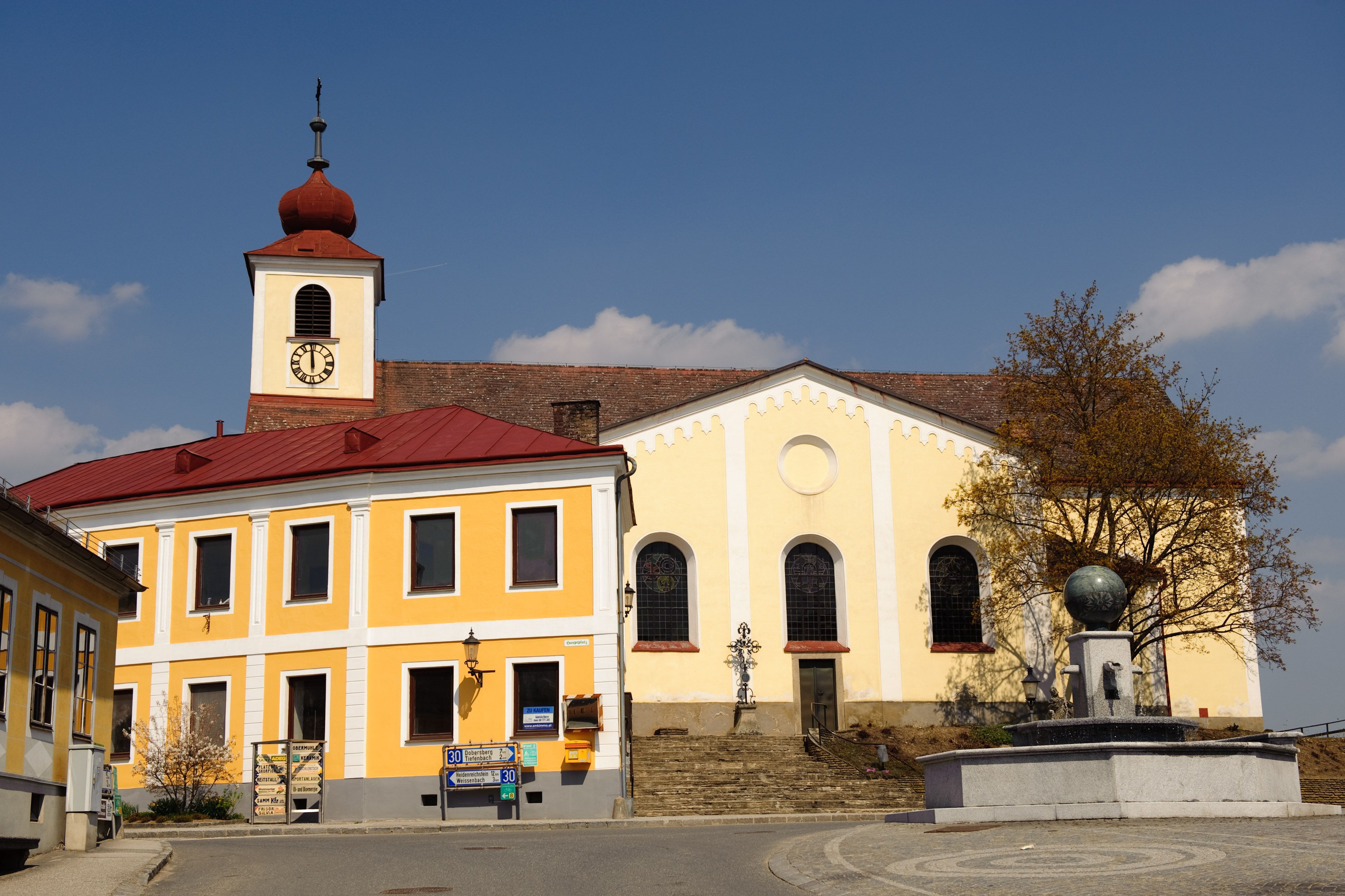 Church with yellow façade and tower with red roof on a main square.