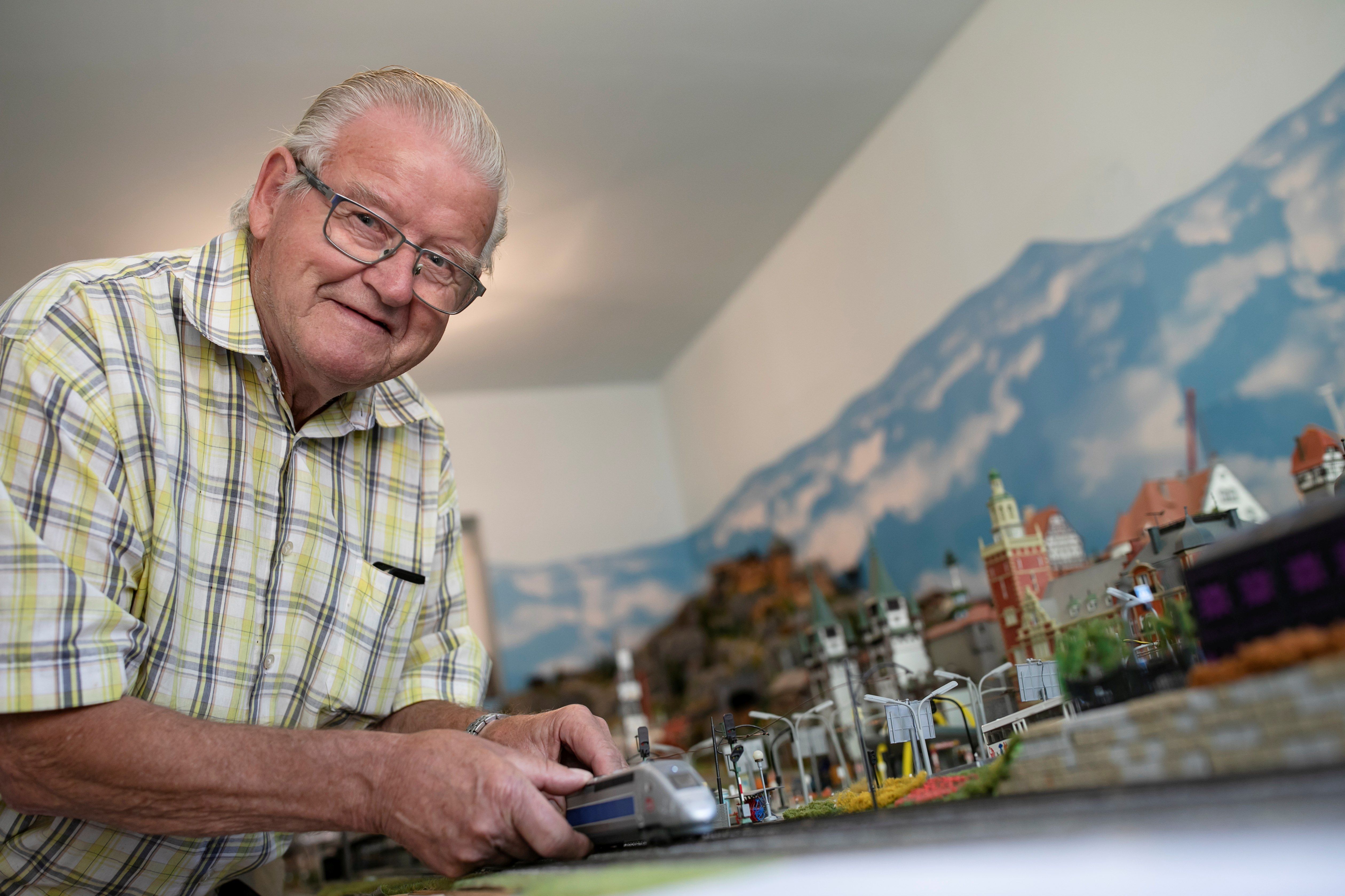 Grandpa Moser is standing in front of his model train layout, pointing to a locomotive. 