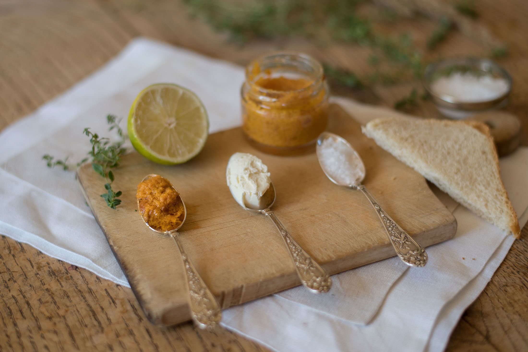 Three spoons with different spreads on a wooden board, next to it half a lime and toast.