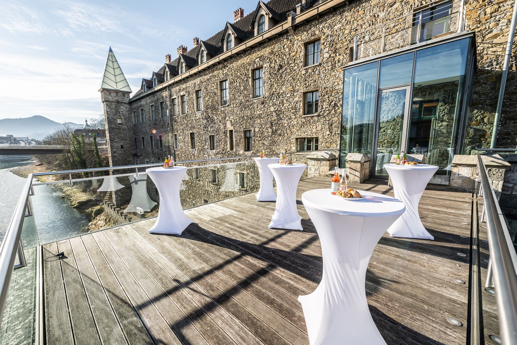 Terrace with bar tables in front of a historic building with a glass façade.