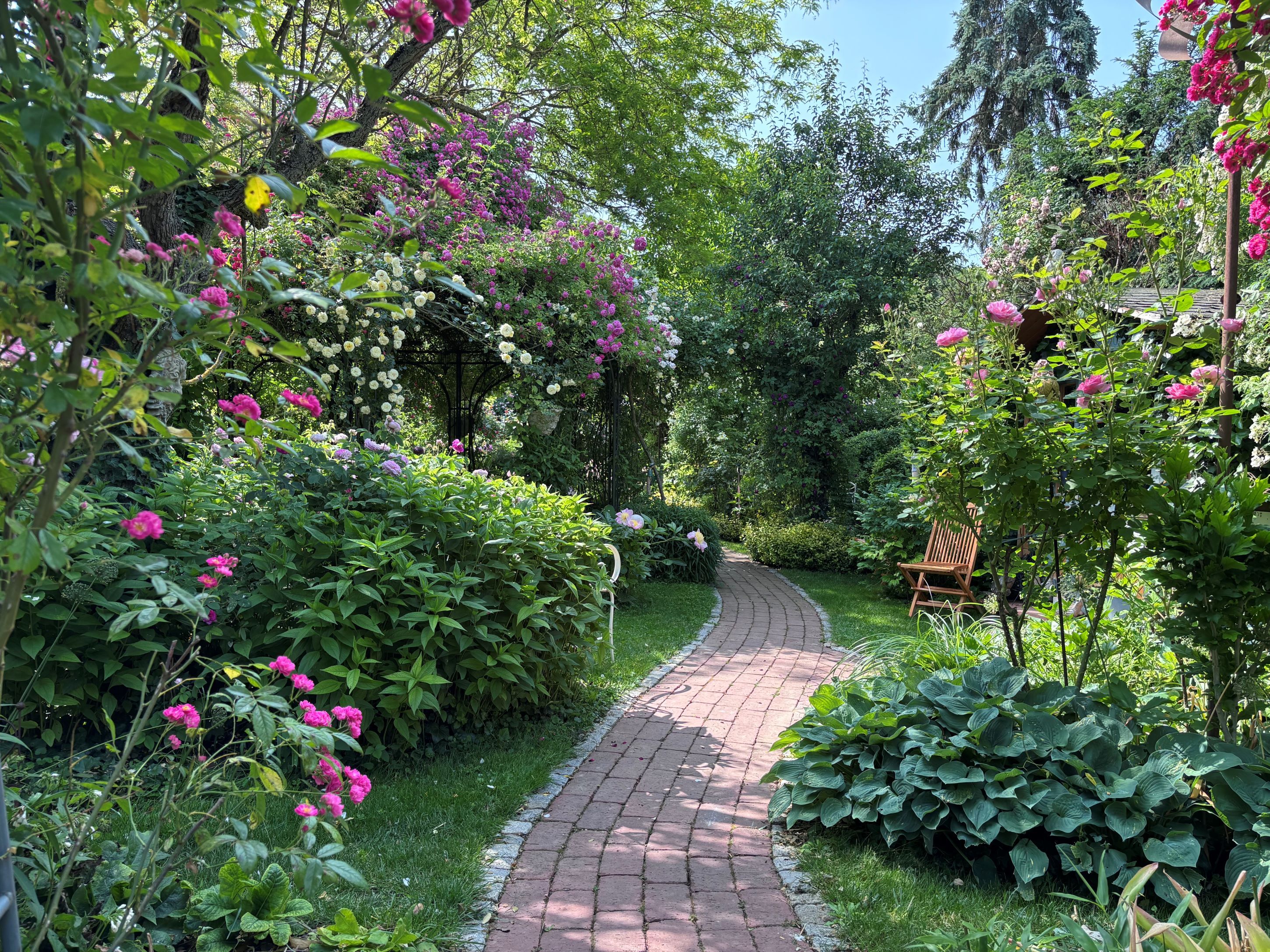 An idyllic garden with a curved brick path surrounded by lush flowers and shrubs.