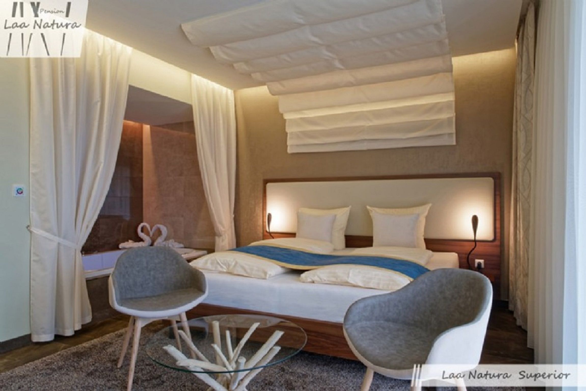 Modern double room with large bed, two gray chairs and a glass table.