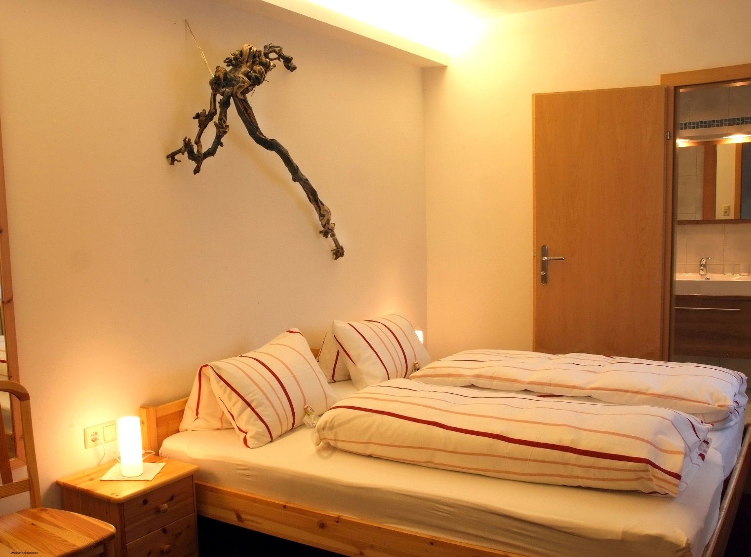 Cozy bedroom with double bed, bedside lamp and grapevine decoration on the wall.