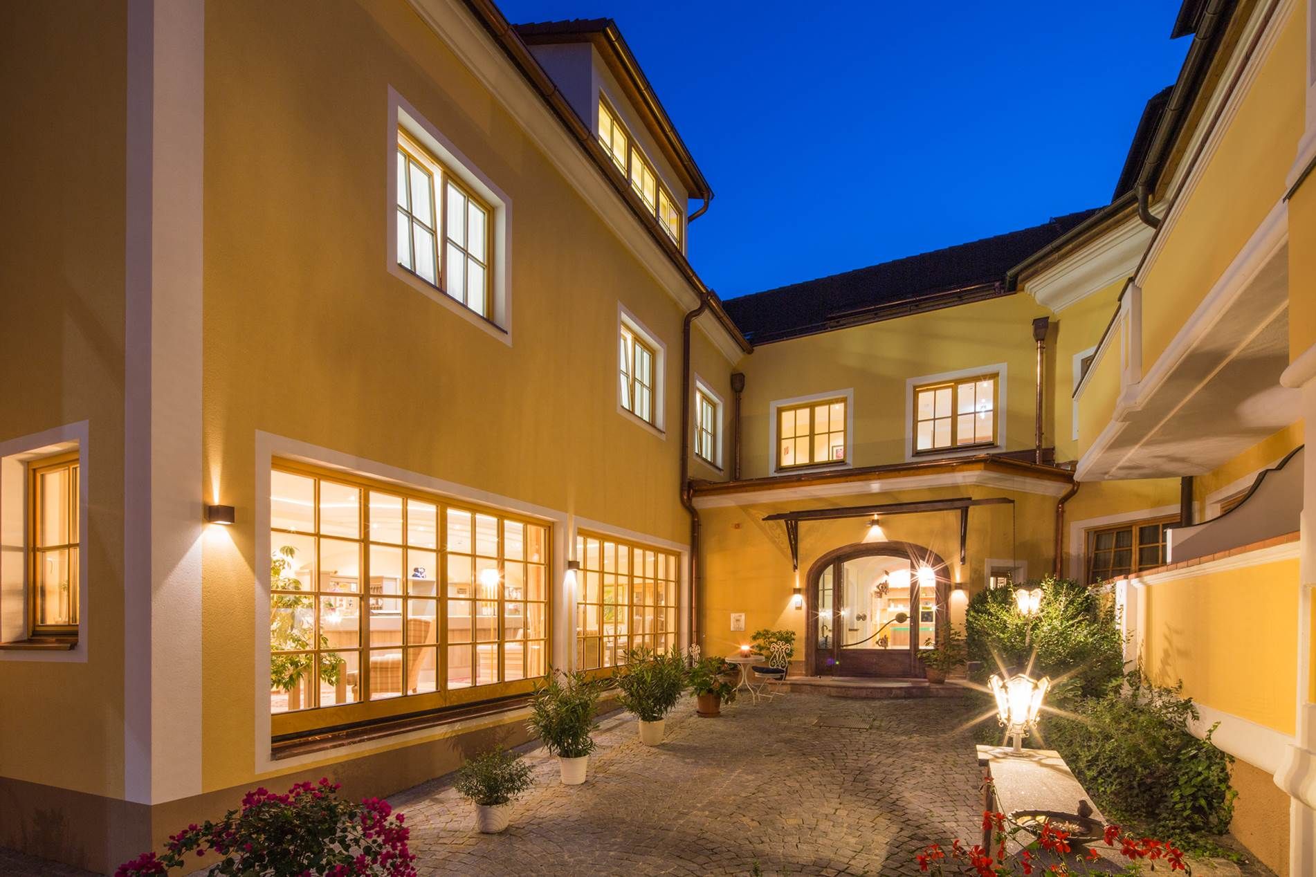 Inner courtyard of the Hotel Zum Schwarzen Bären with illuminated windows and plants at night.