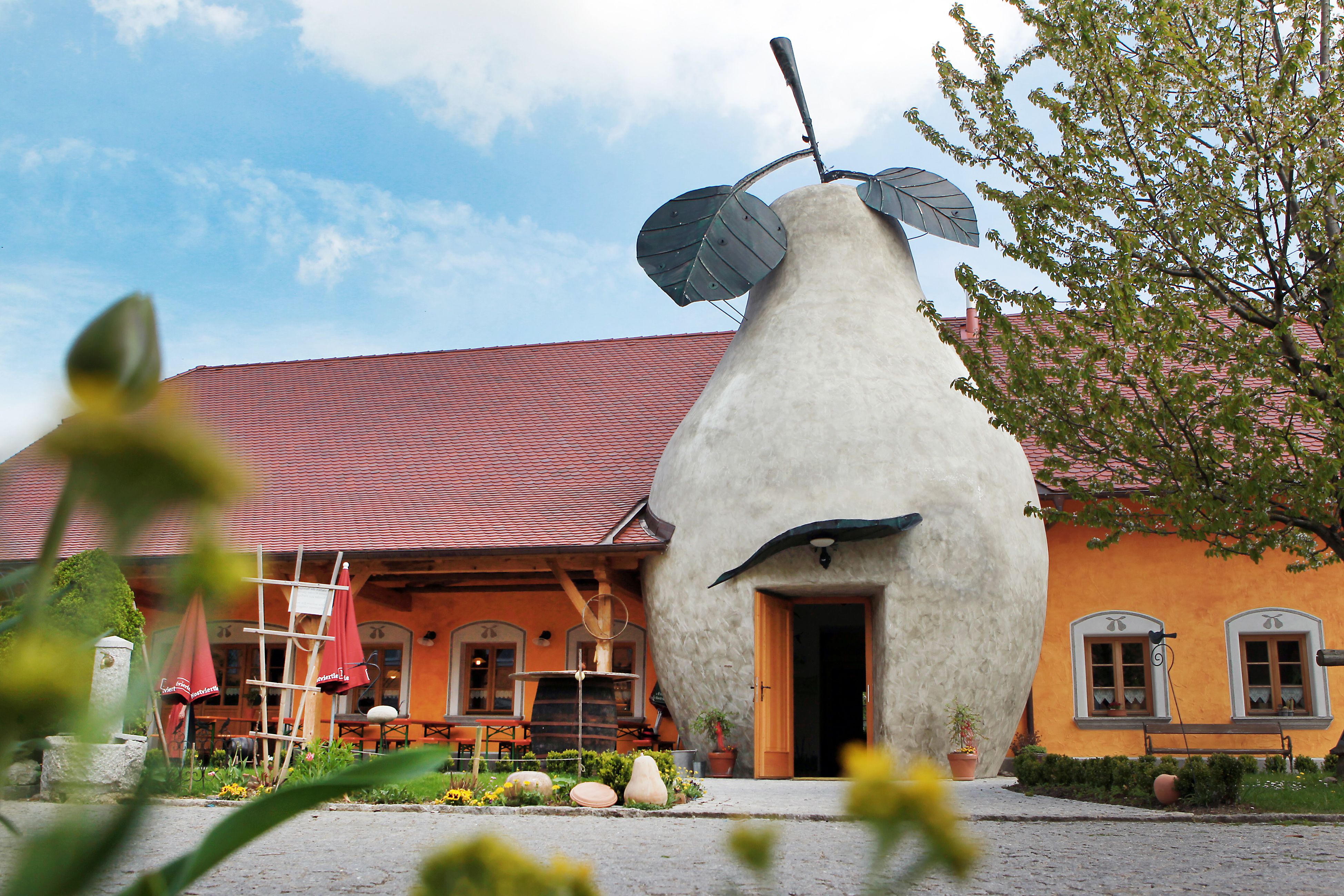 Building with pear-shaped entrance and red roof, surrounded by plants.