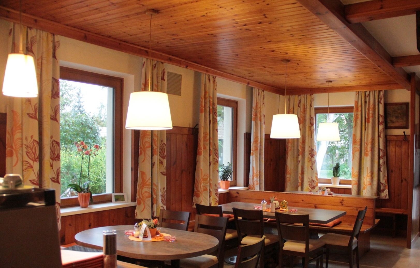 Cozy dining room with wooden furniture, large windows and hanging lamps.