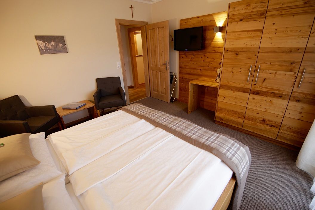 Bedroom with double bed, wooden furniture and TV on the wall.
