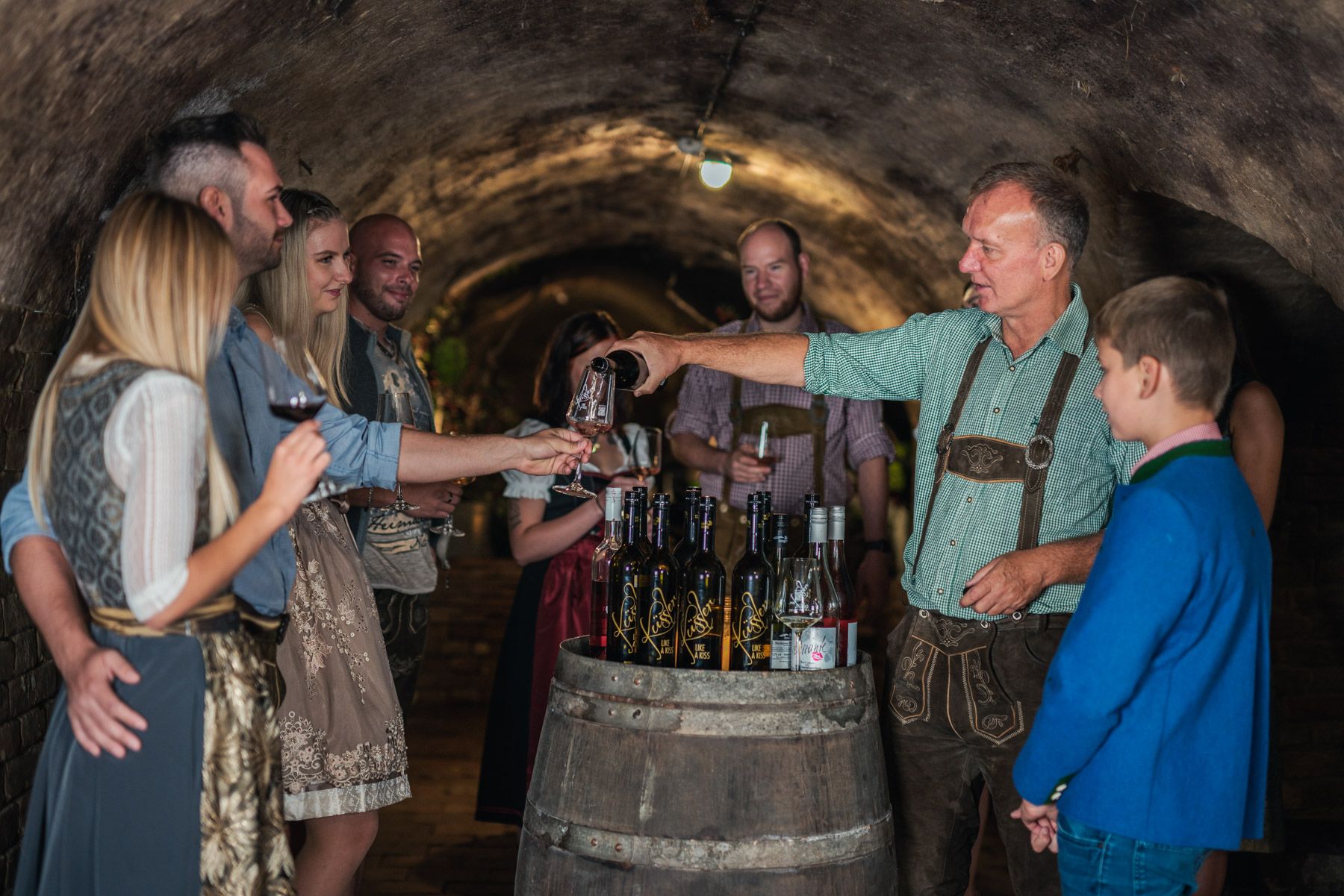 A group of people in traditional dress at a wine tasting in a wine cellar.