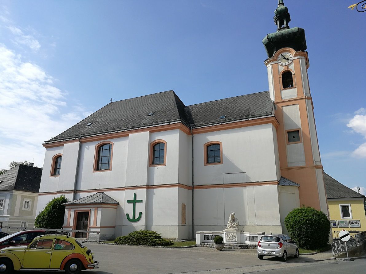 Würmla parish church with clock tower and parked cars.