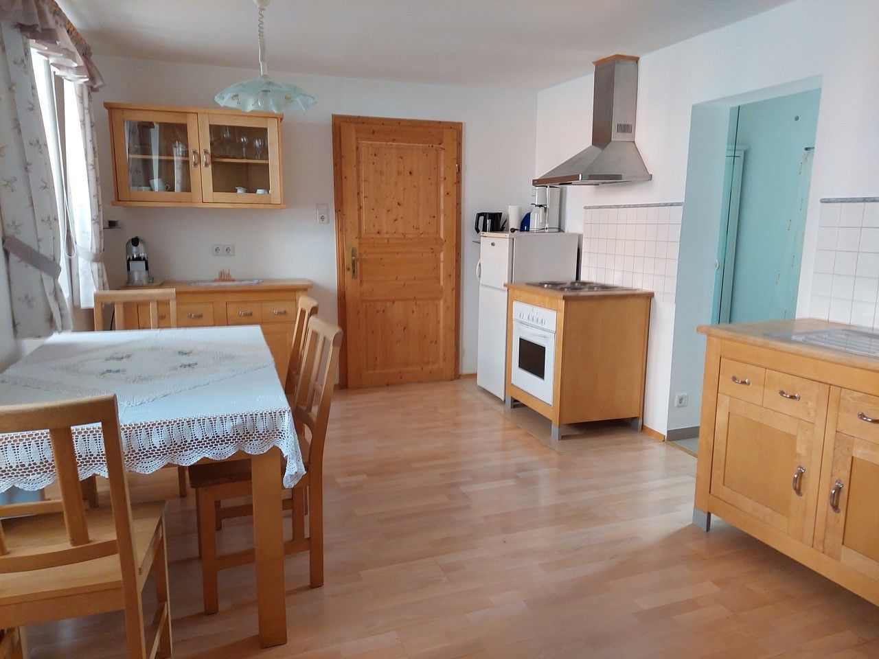 Kitchen with wooden furniture, dining table, chairs, stove, fridge and wall cupboard.