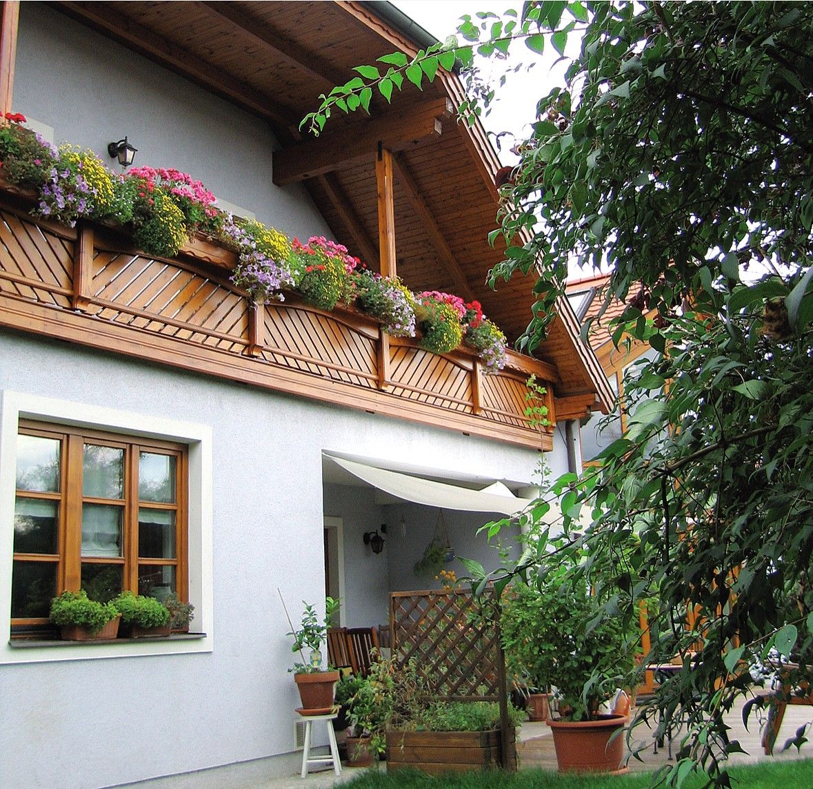 A guest house with a wooden balcony and blooming flowers, surrounded by green plants.