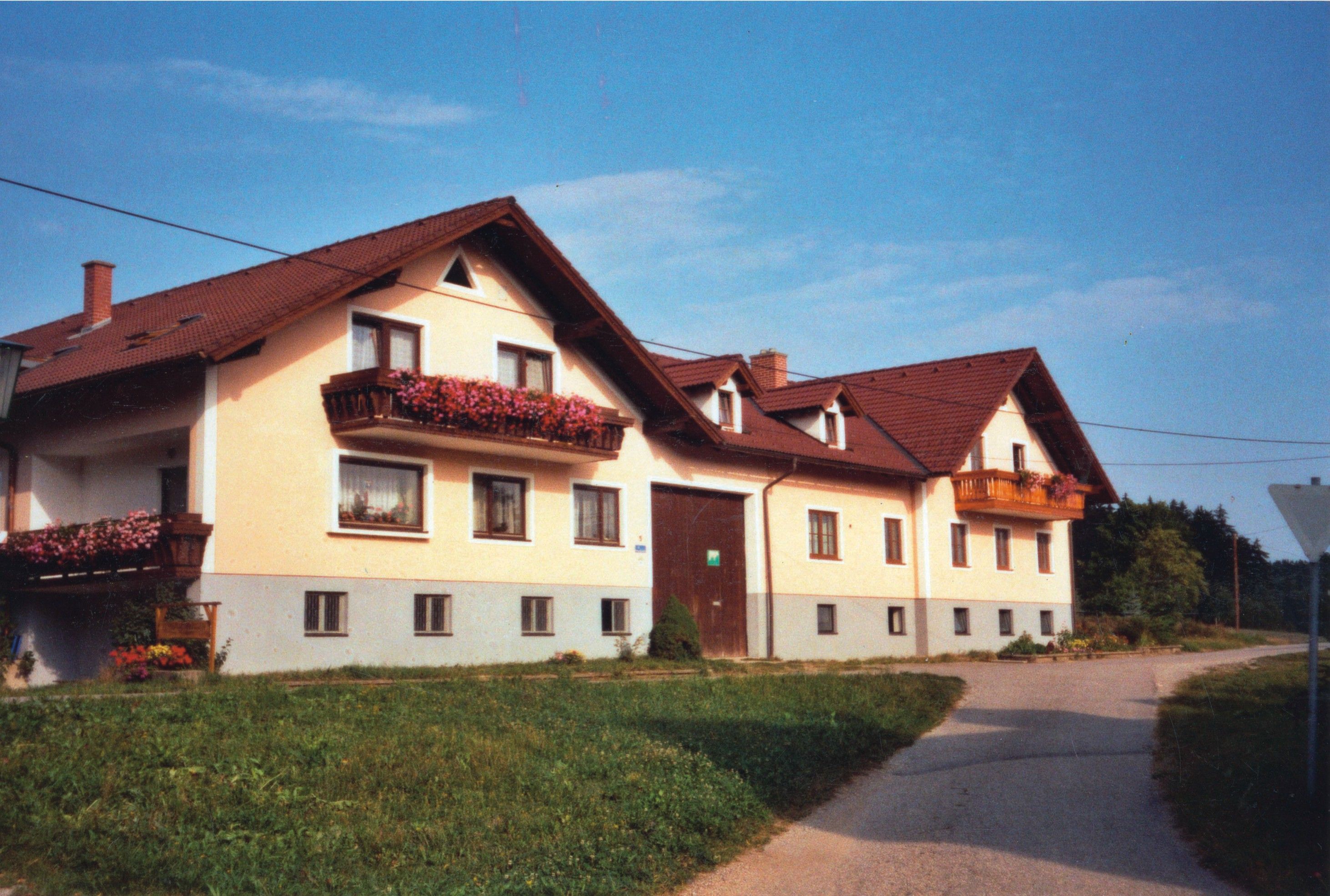 A large, two-storey farmhouse with red roofs and flower boxes on the balconies.