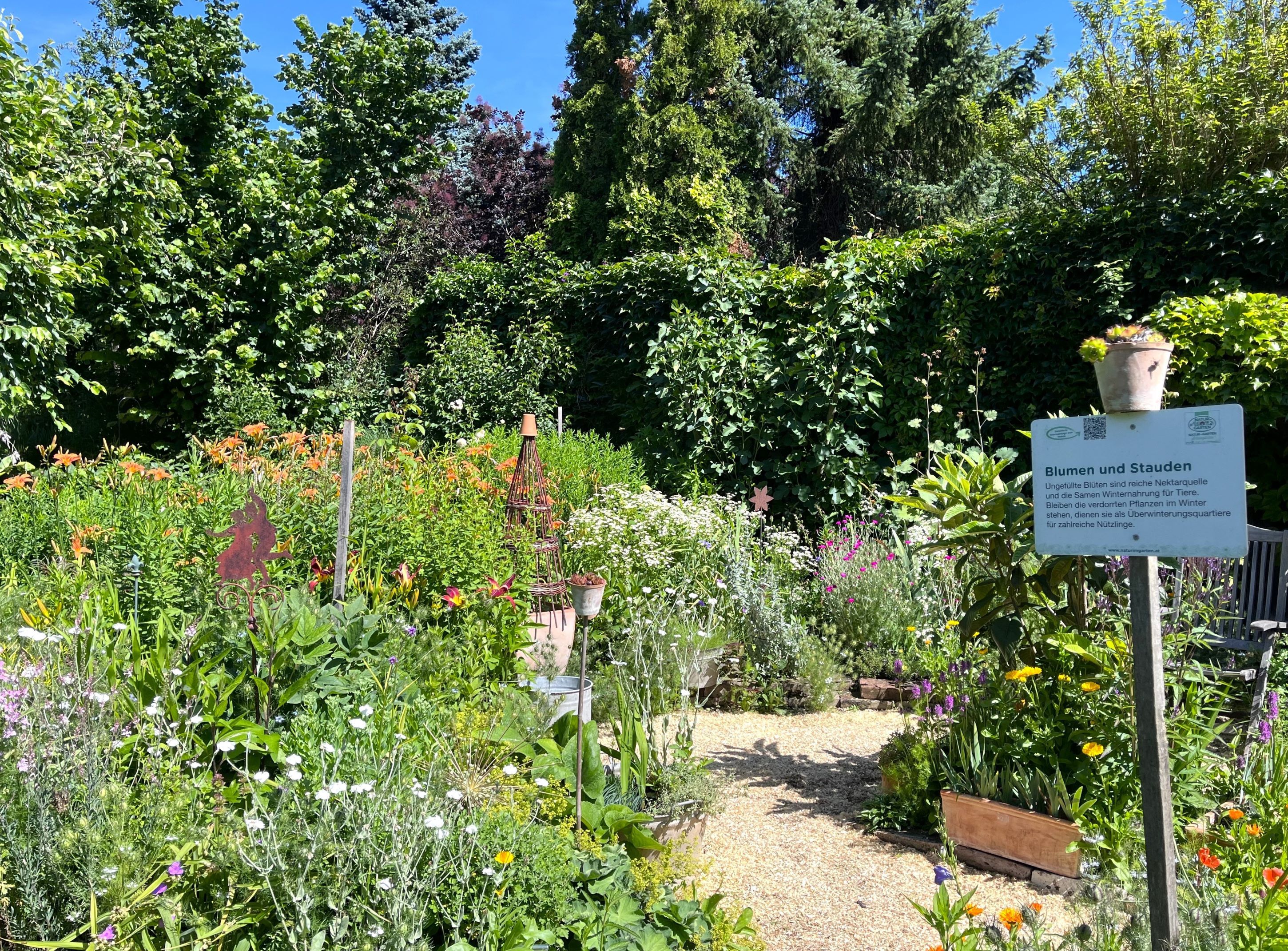 A colorful cottage garden with various flowers and a sign describing "flowers and perennials".