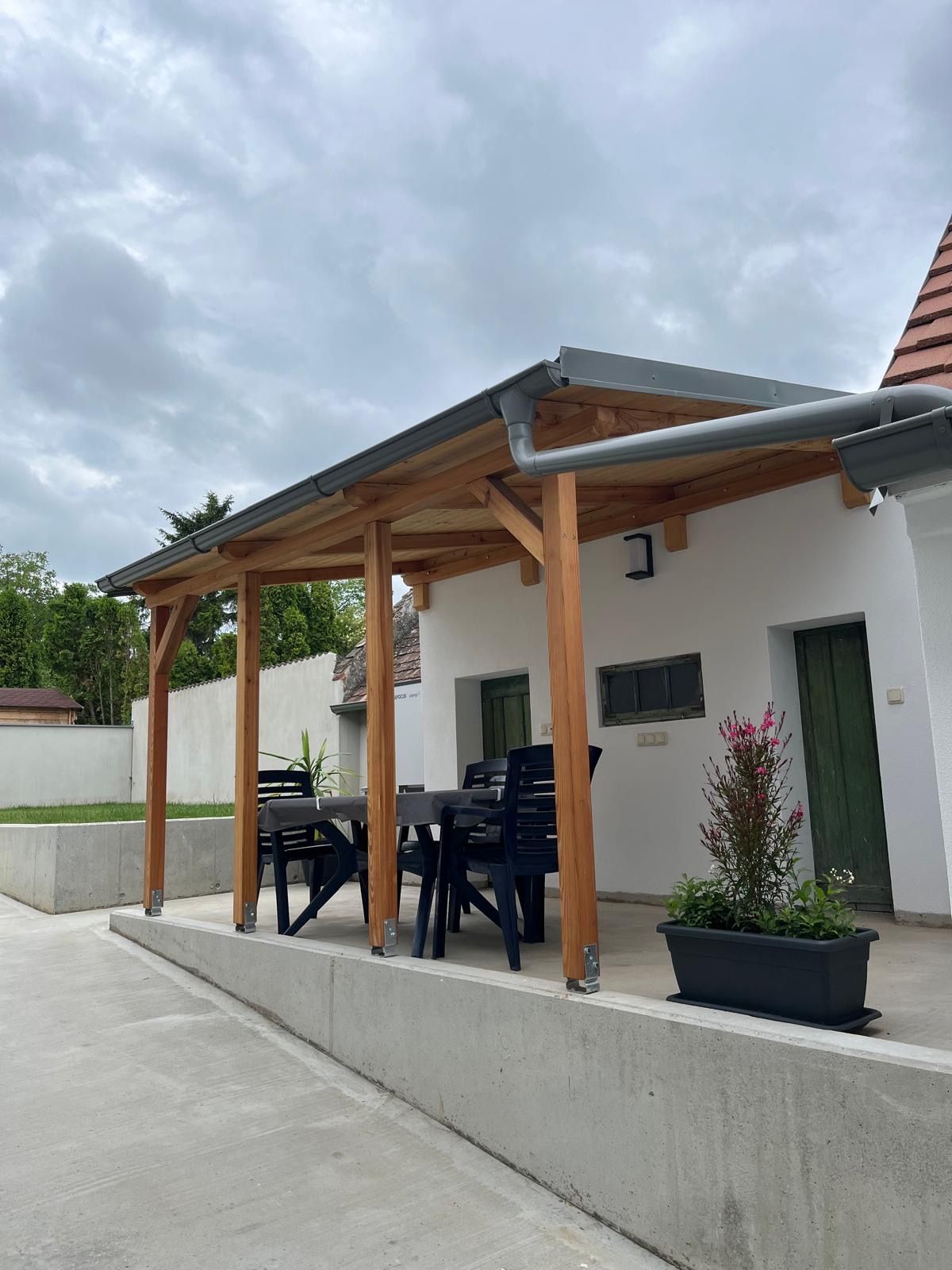 Covered terrace with table and chairs, surrounded by plants.