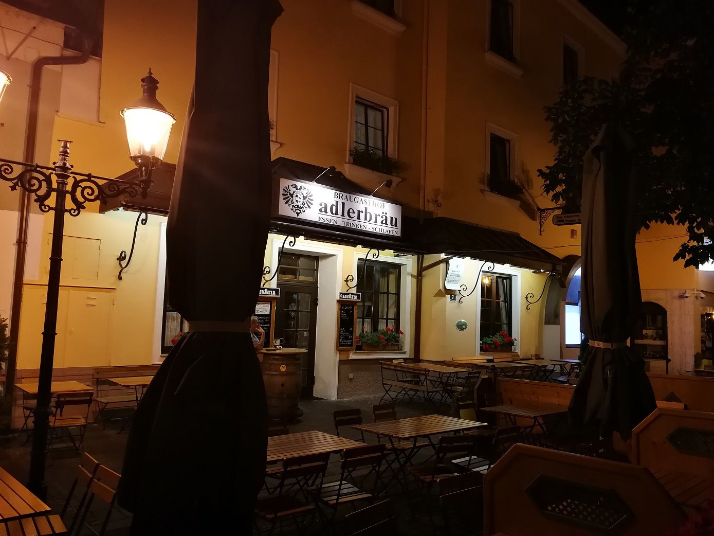 Night shot of a restaurant with the sign 'Adlerbräu' and empty tables outside.