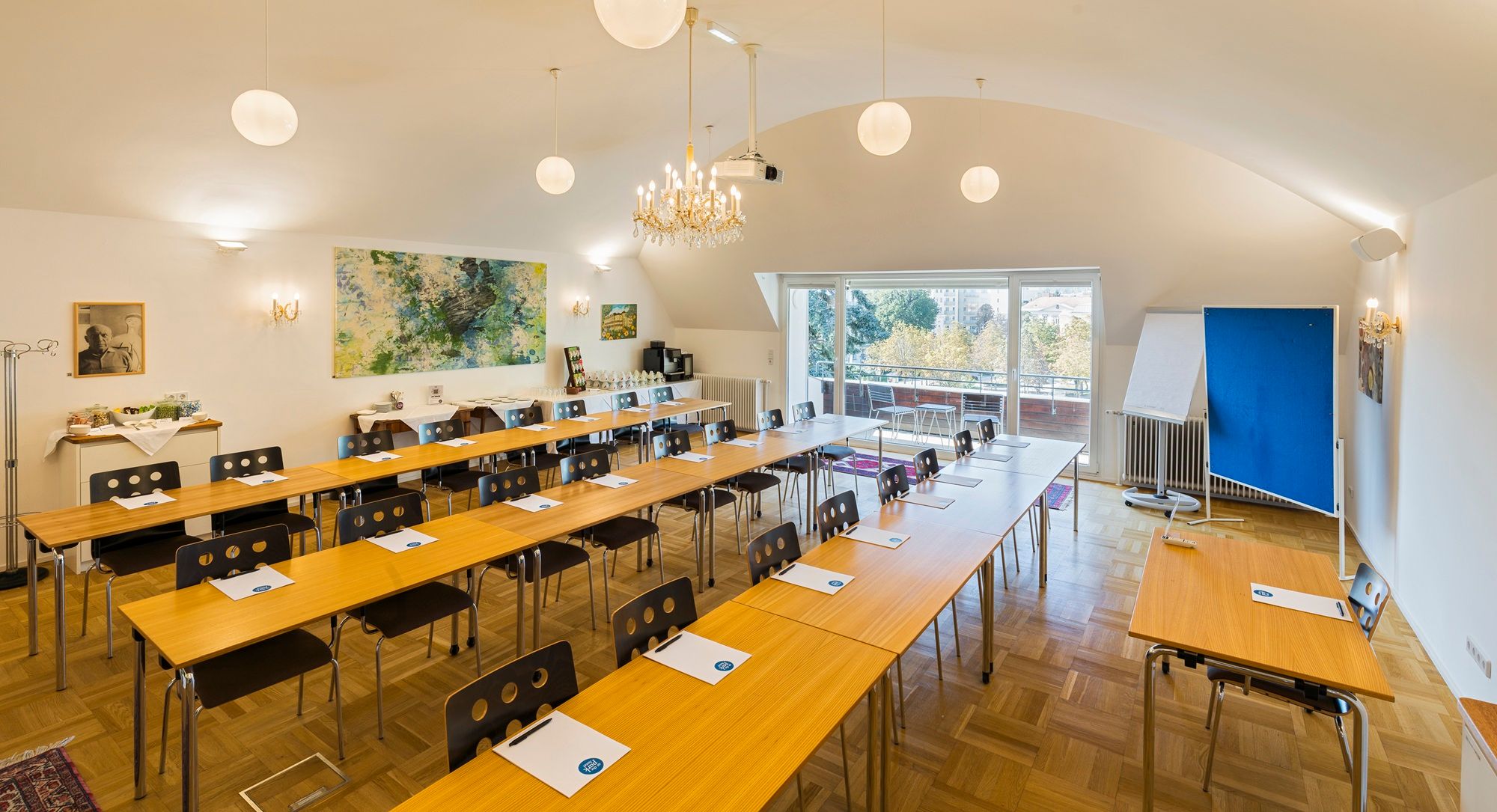 A conference room with tables and chairs, a chandelier and a large window with a view outside.